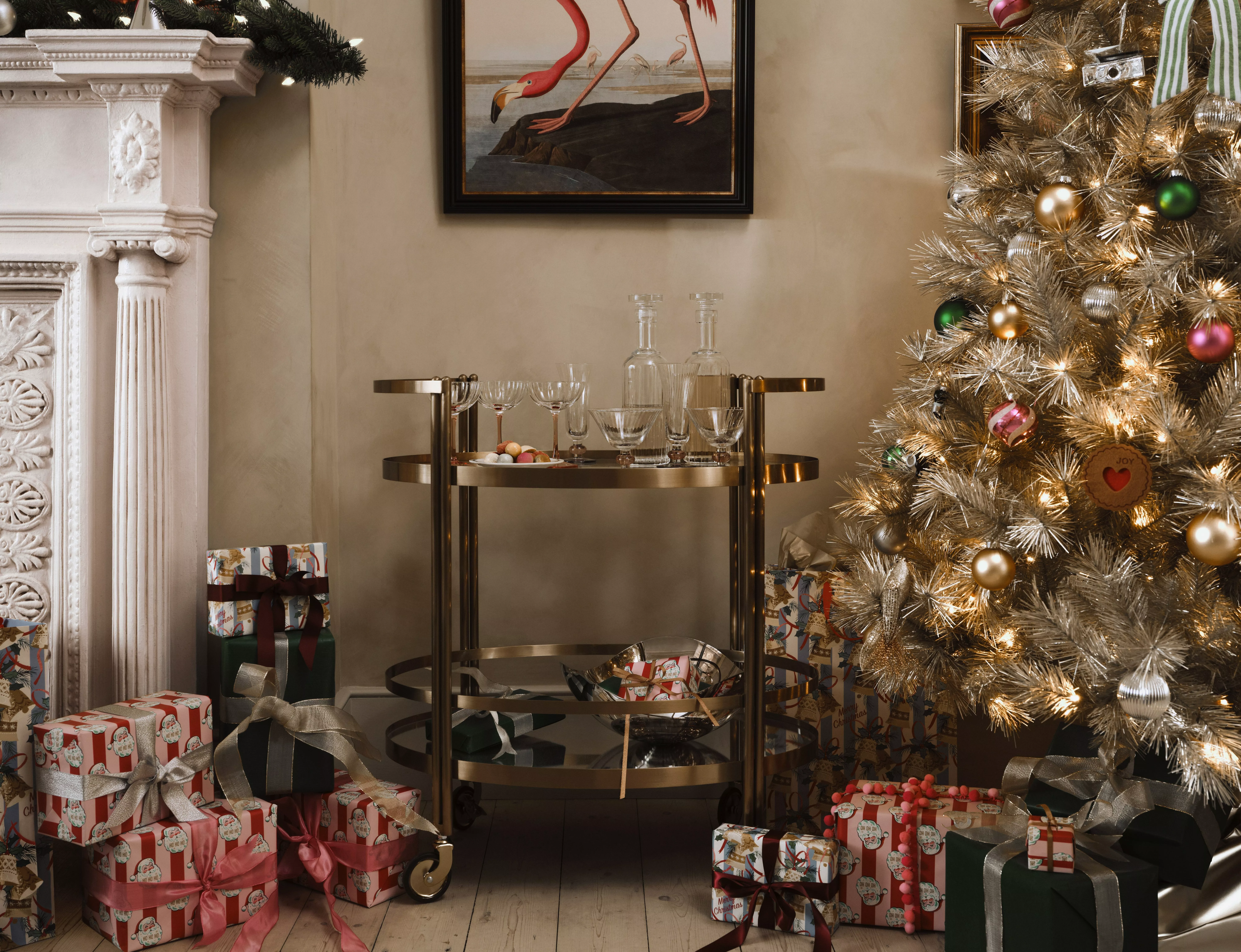 Christmas tree with fairy lights and decorations next to a glass drinks trolley with presents under the tree