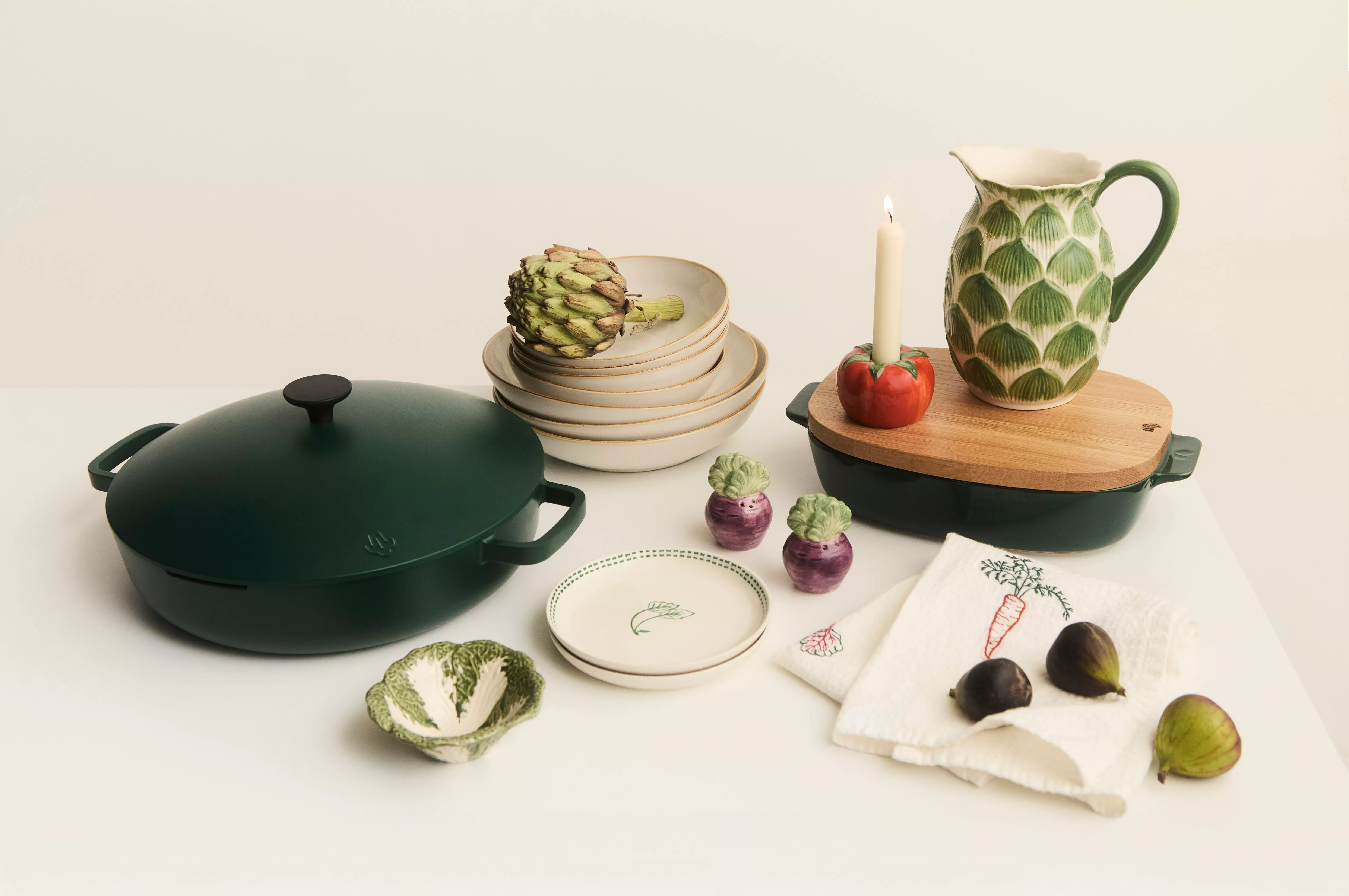 Green pan next to stacked bowls and plates. Tomato shaped candle holder, lettuce shaped dish and leaf patterned jug. 
