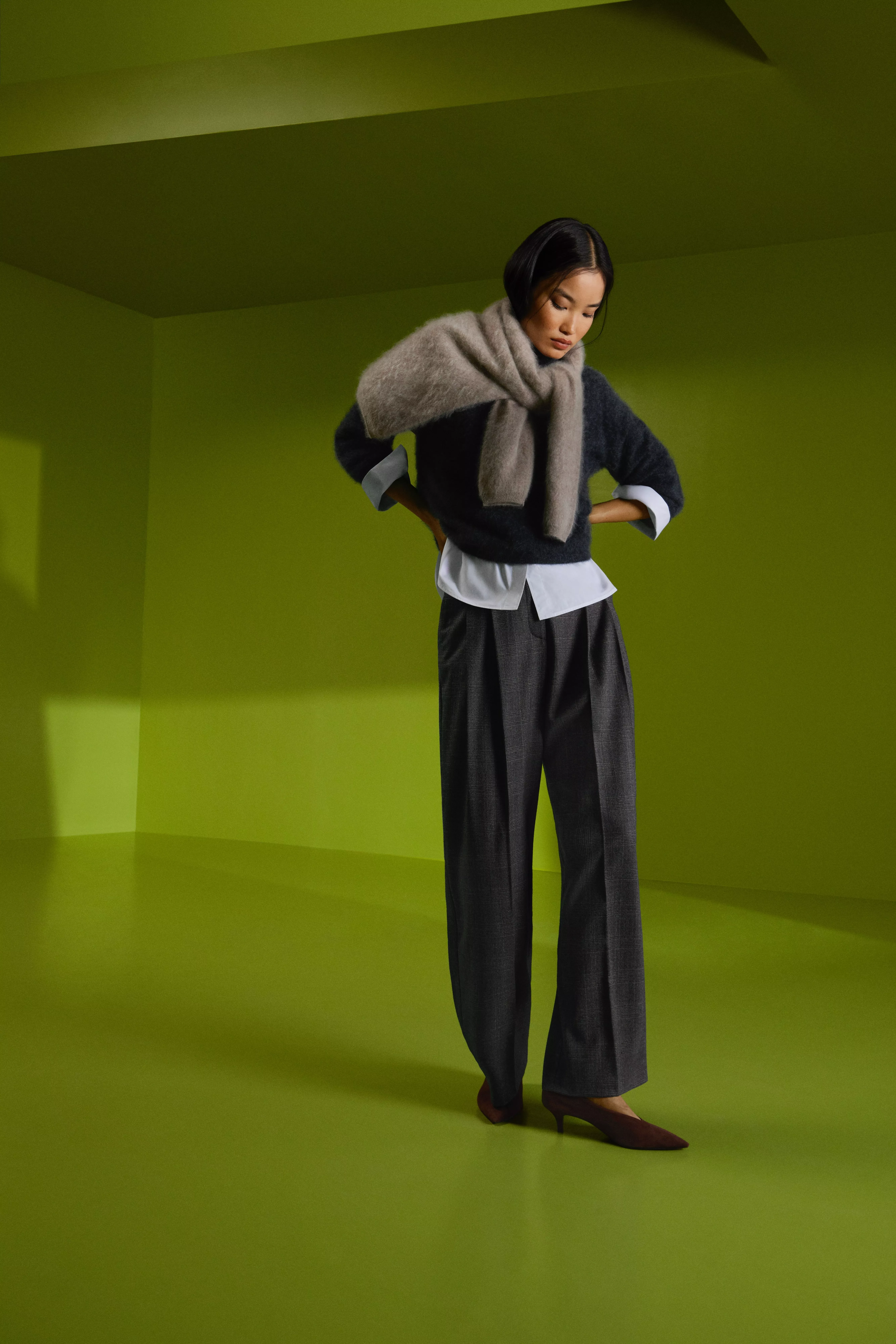 Fashion model in grey knit jumper and oversized scarf with tailored trousers, studio shot on green backdrop