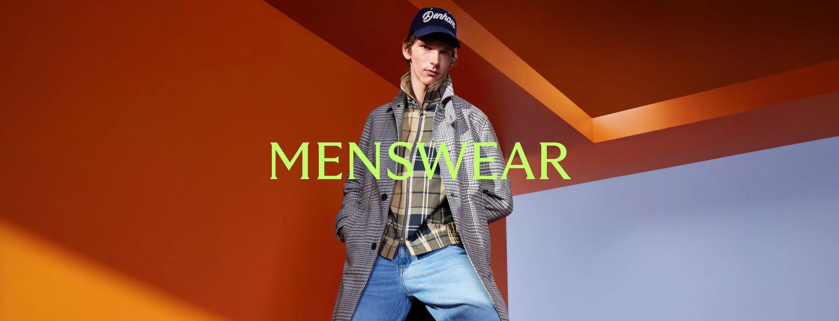 Men’s menswear fashion banner with model in checked coat, cap and jeans against bold orange geometric backdrop
