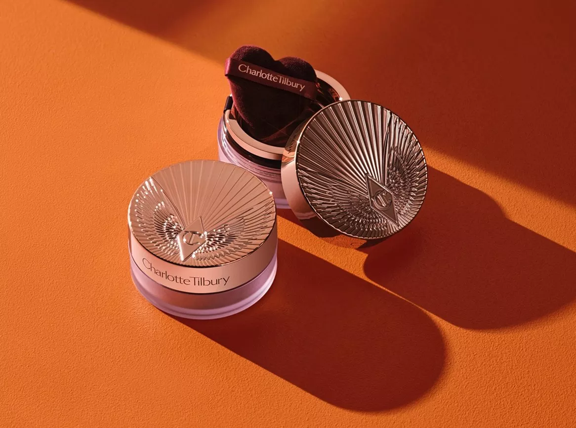 Charlotte Tilbury rose gold compact powder with puff applicator on orange background, studio lighting shadows