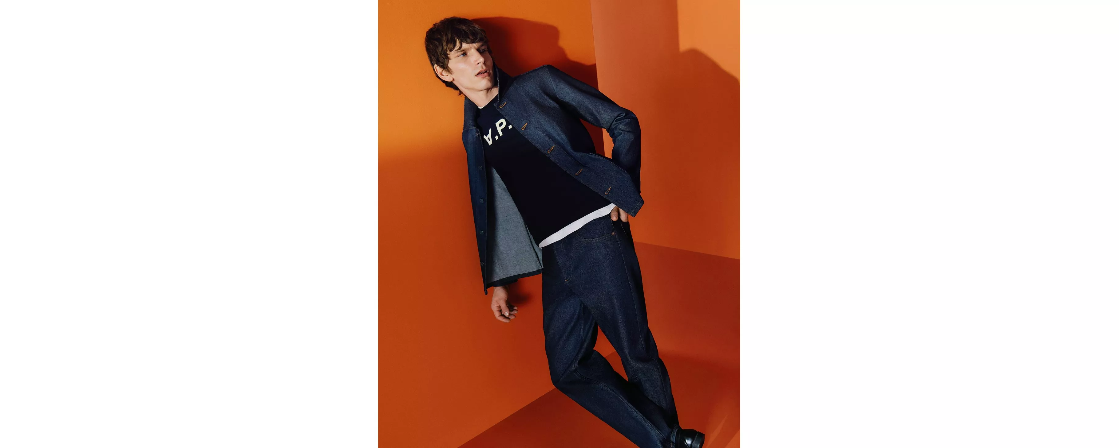 Men’s denim jacket and jeans with black sweatshirt, fashion model posing against a bold orange studio backdrop