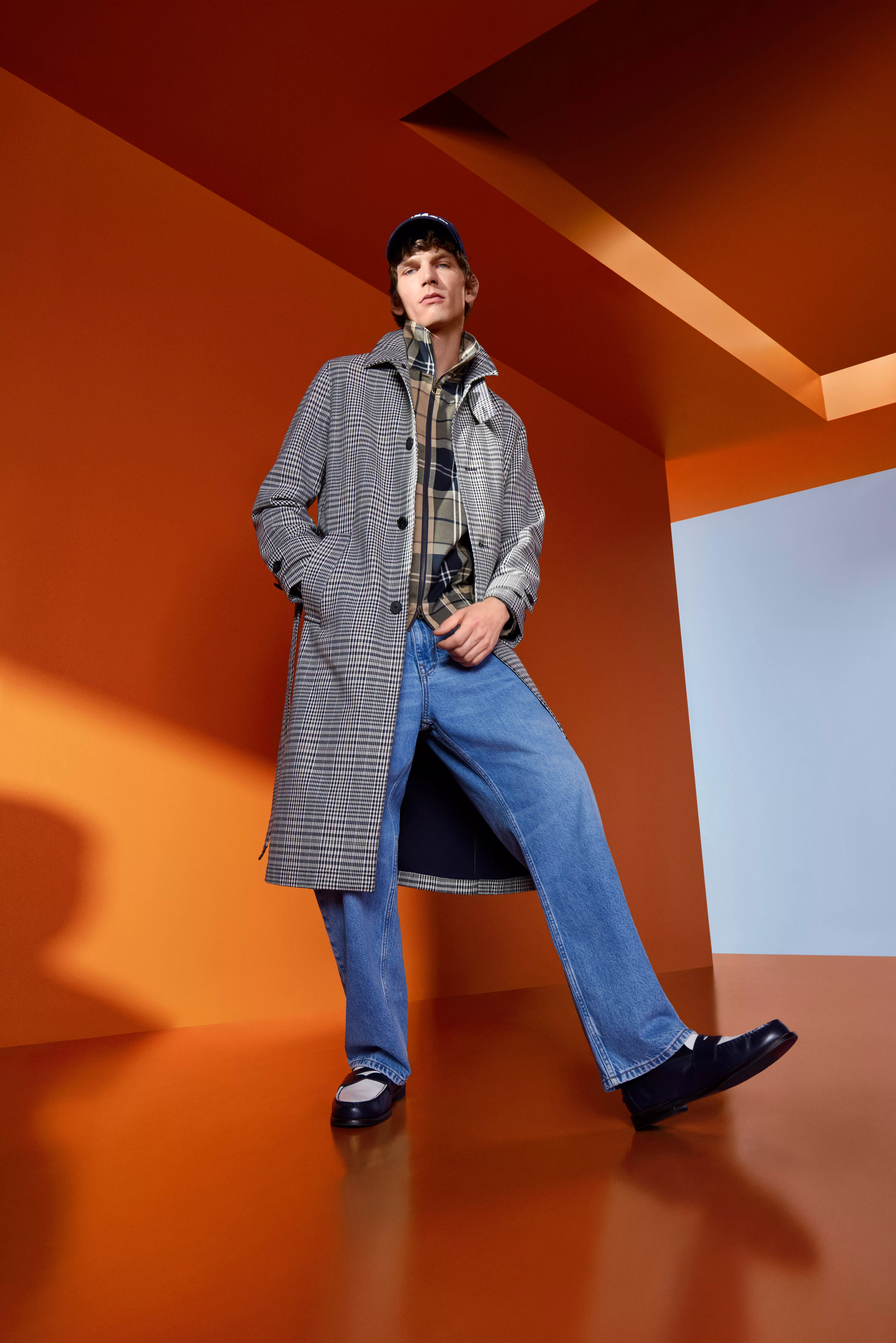 Fashion model in navy and tan varsity jacket with grey trousers, posing in studio with green backdrop