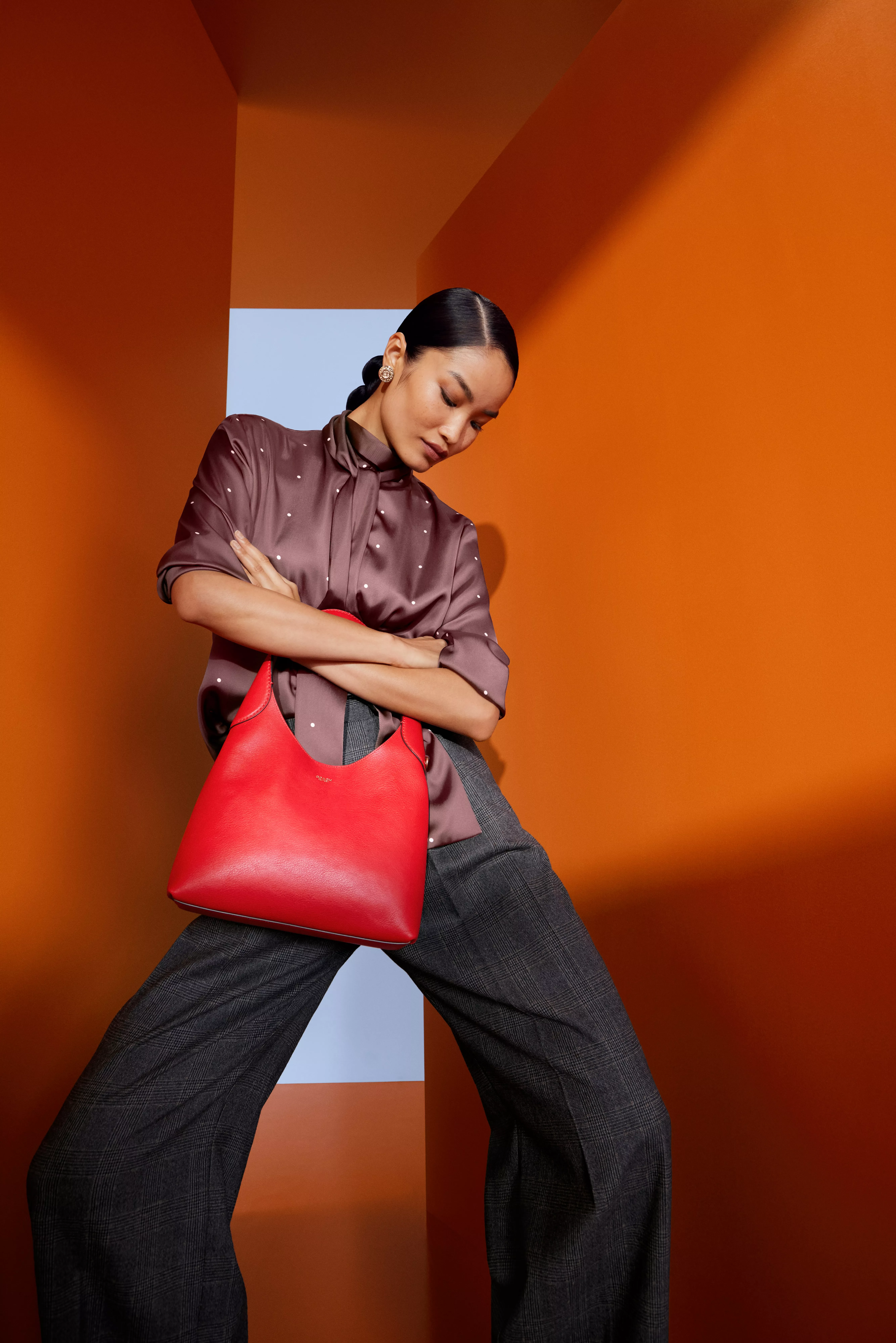 Woman in a brown blouse and trousers, carrying a red shoulder bag