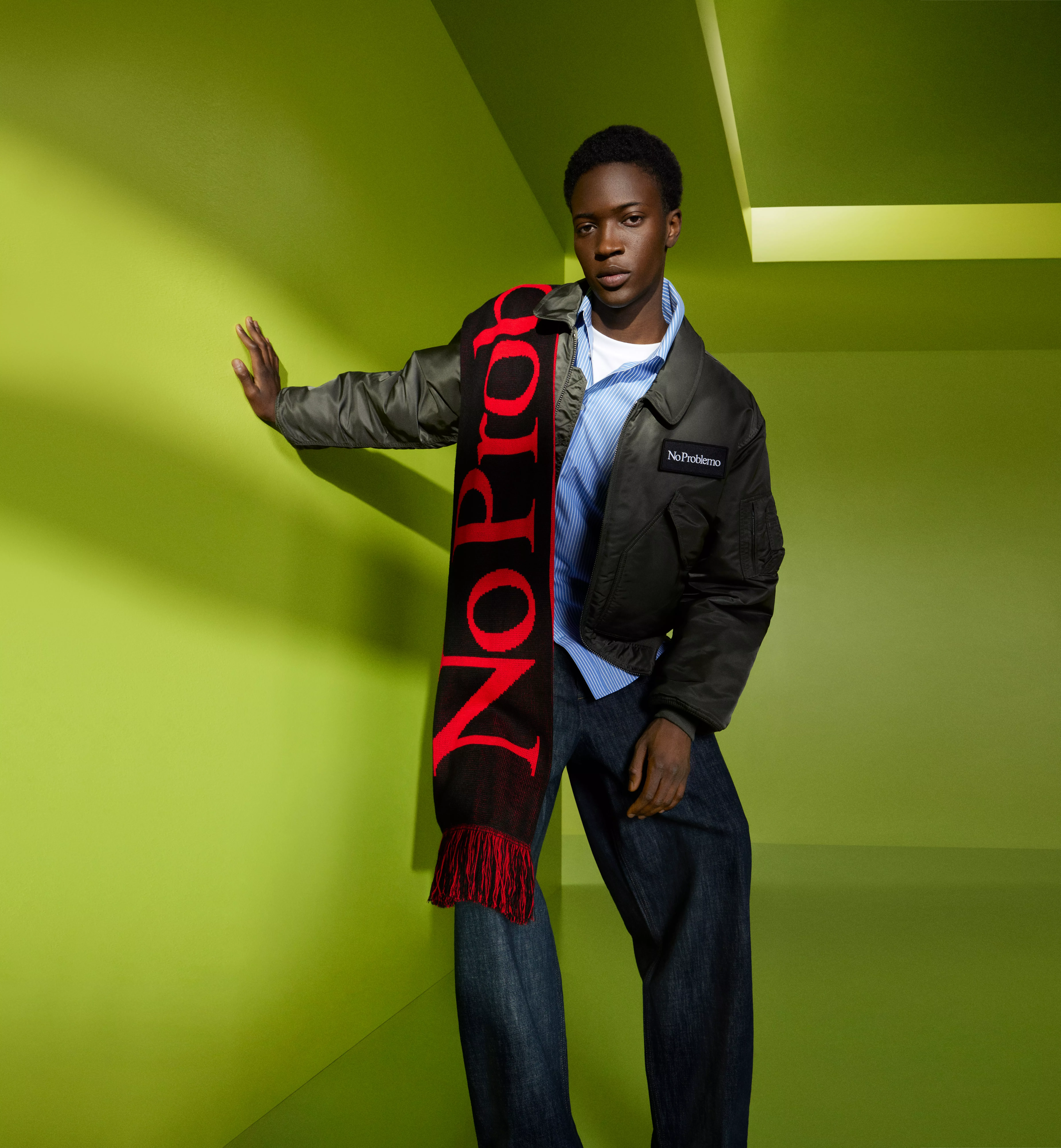 Fashion model in bomber jacket and oversized red logo scarf, posing in a lime green studio set
