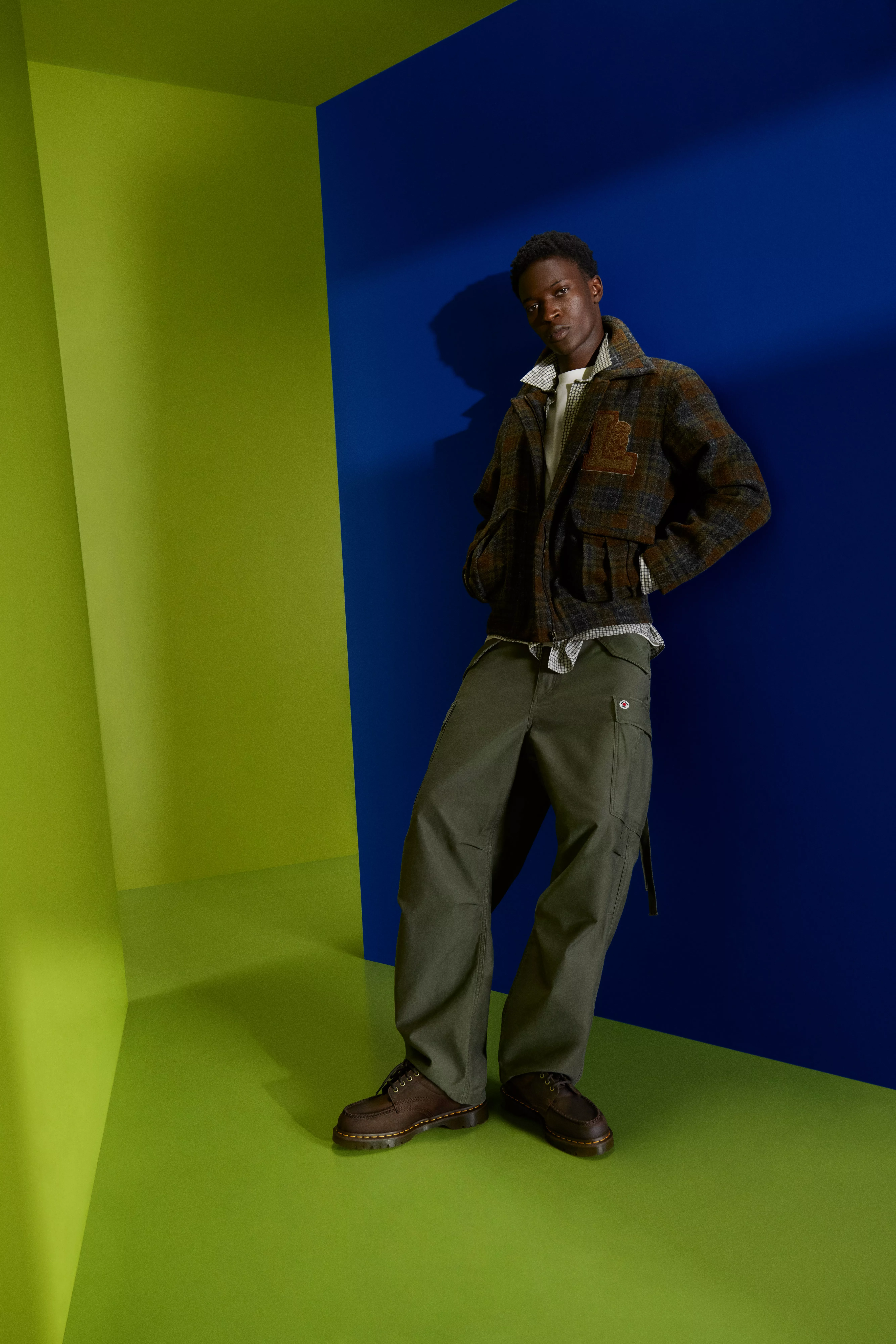 Fashion model in plaid jacket and olive cargo trousers, posing in studio with bold blue and green backdrop