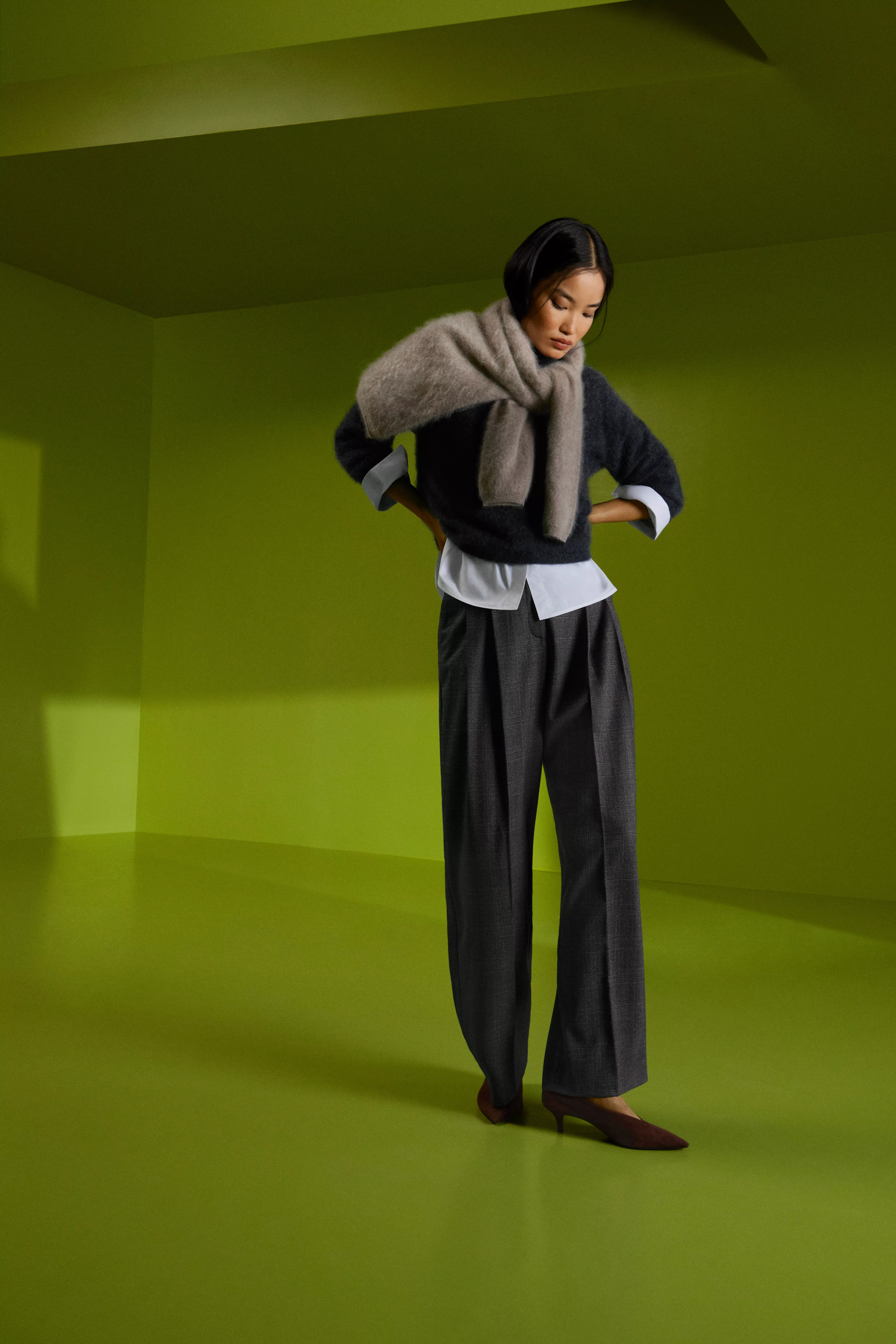 Fashion model in grey knit jumper and scarf with wide-leg trousers, posing in a lime-green studio setting