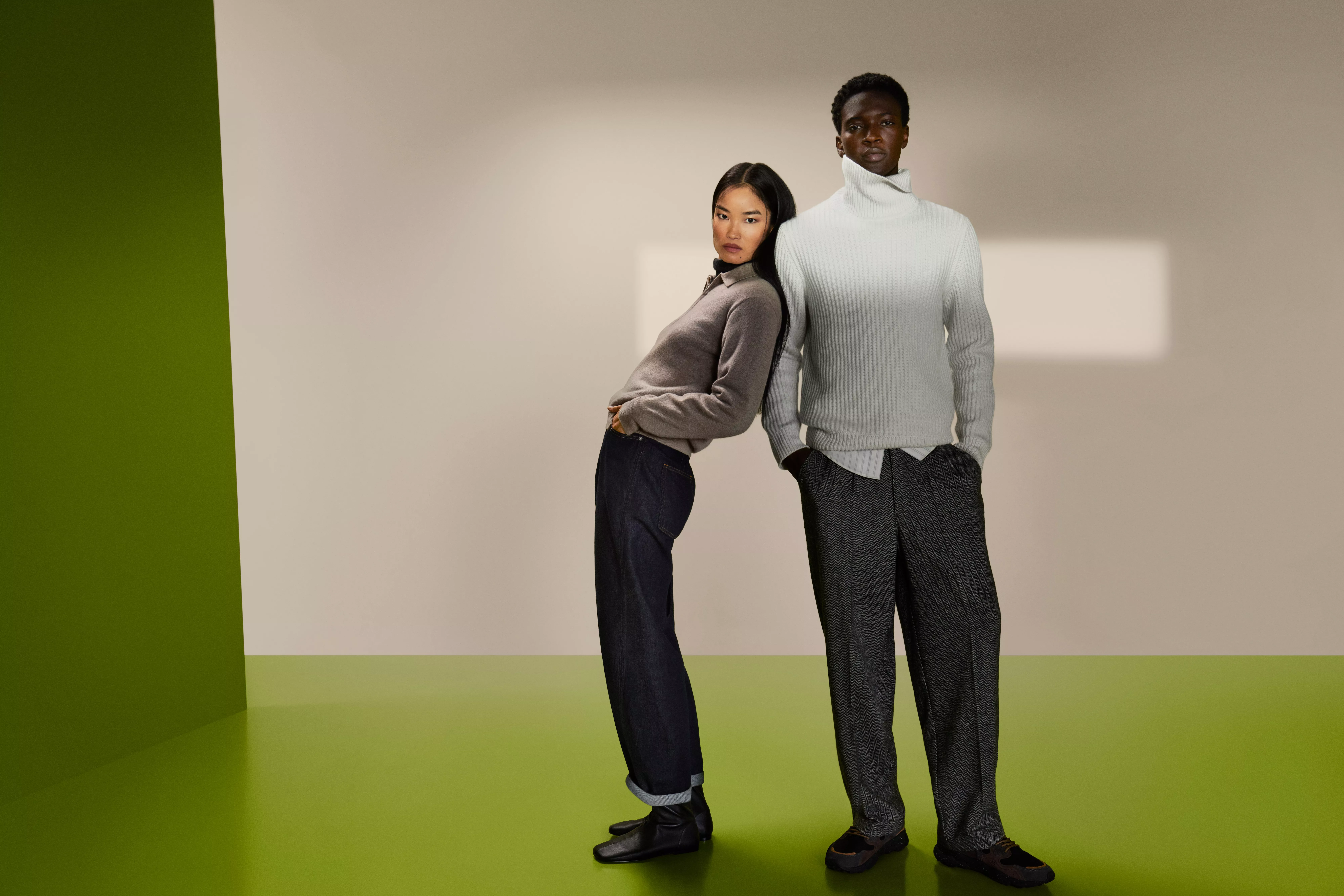 Woman wearing a taupe half zip cashmere jumper, leaning against a man wearing an ecru roll neck cashmere jumper