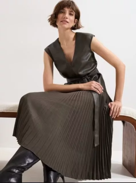 Woman modelling pleated midi dress with leather-look bodice and belt, styled with black knee-high boots indoors