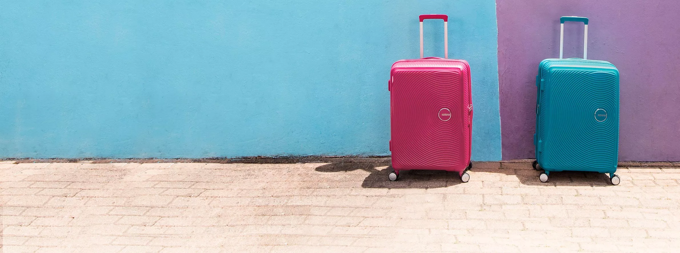 two american tourister brand suitcases, one pink and the other blue