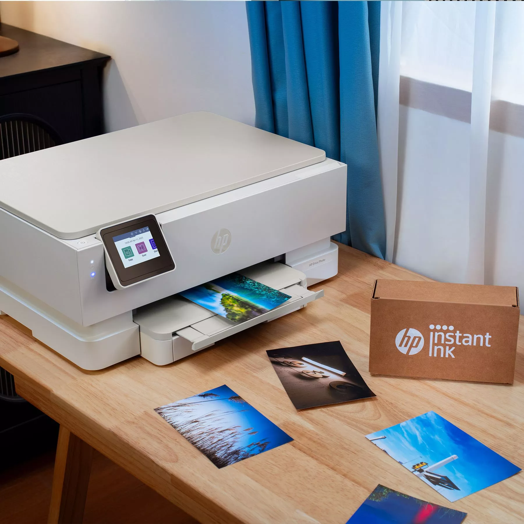 A modern HP printer on a wooden desk, surrounded by vibrant photo prints and an HP Instant Ink box.