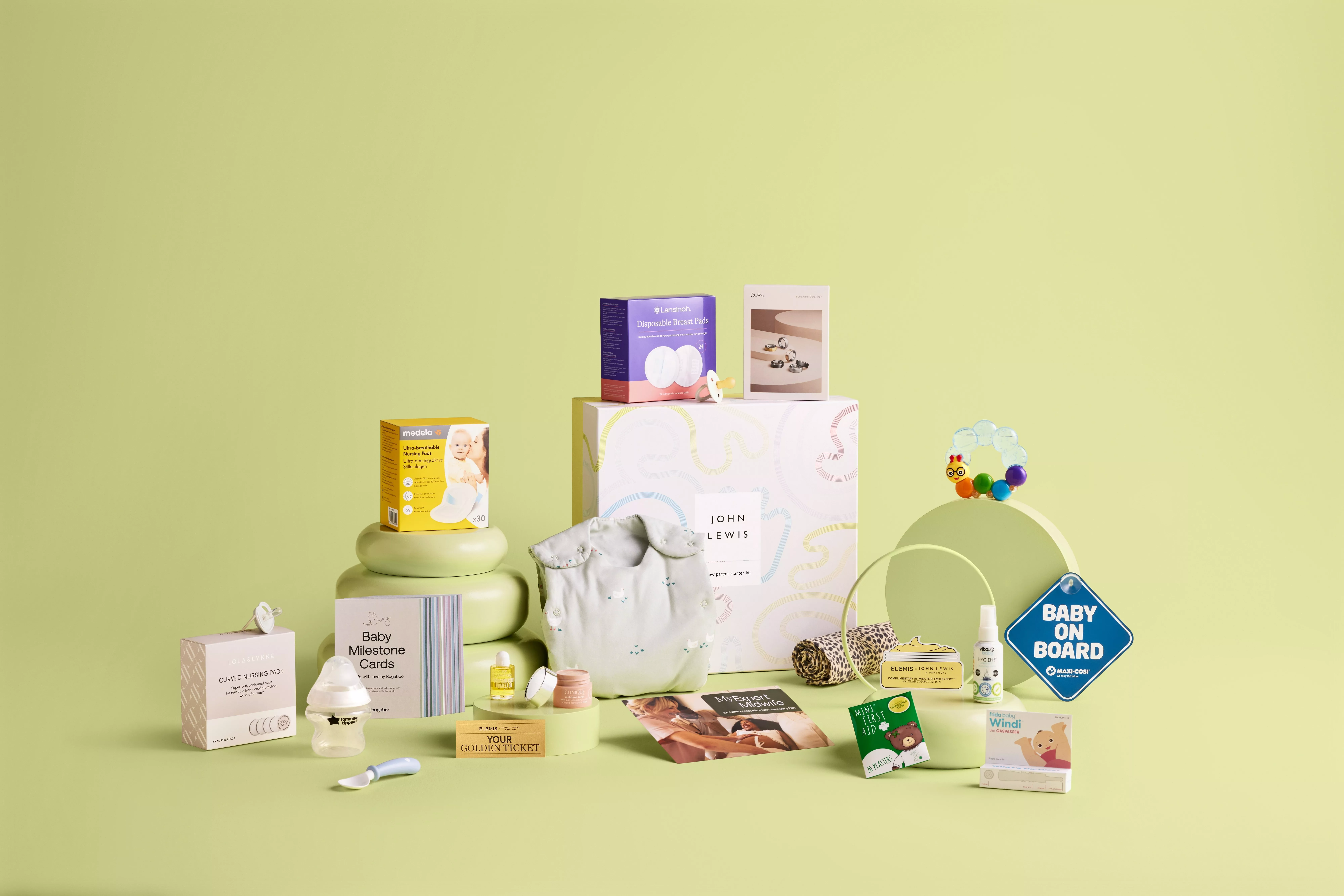 A collection of baby essentials is displayed, featuring nursing pads, baby clothes, and milestone cards on a pastel backdrop.