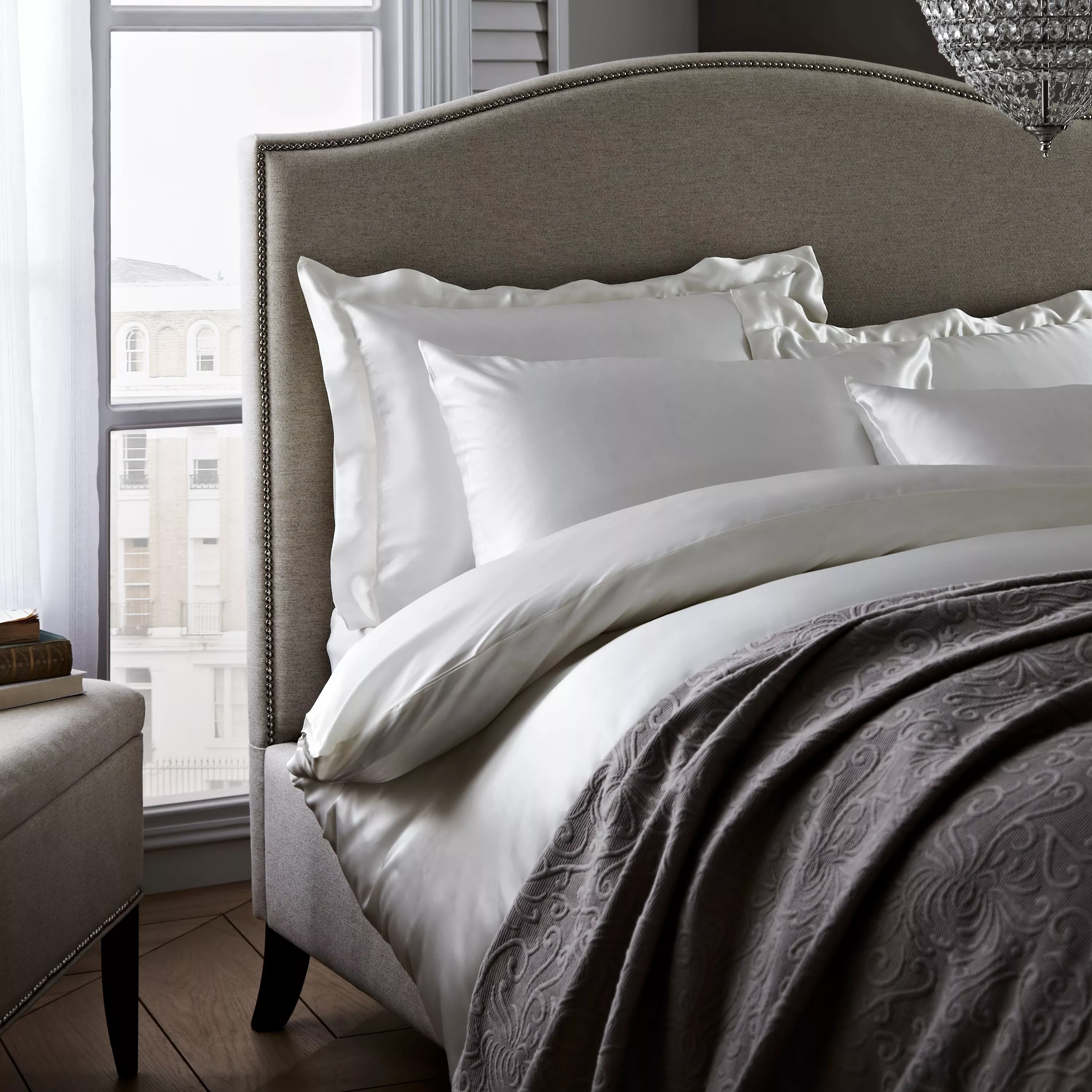 Luxury upholstered bed with curved headboard, crisp white bedding and grey throw in elegant bedroom by window