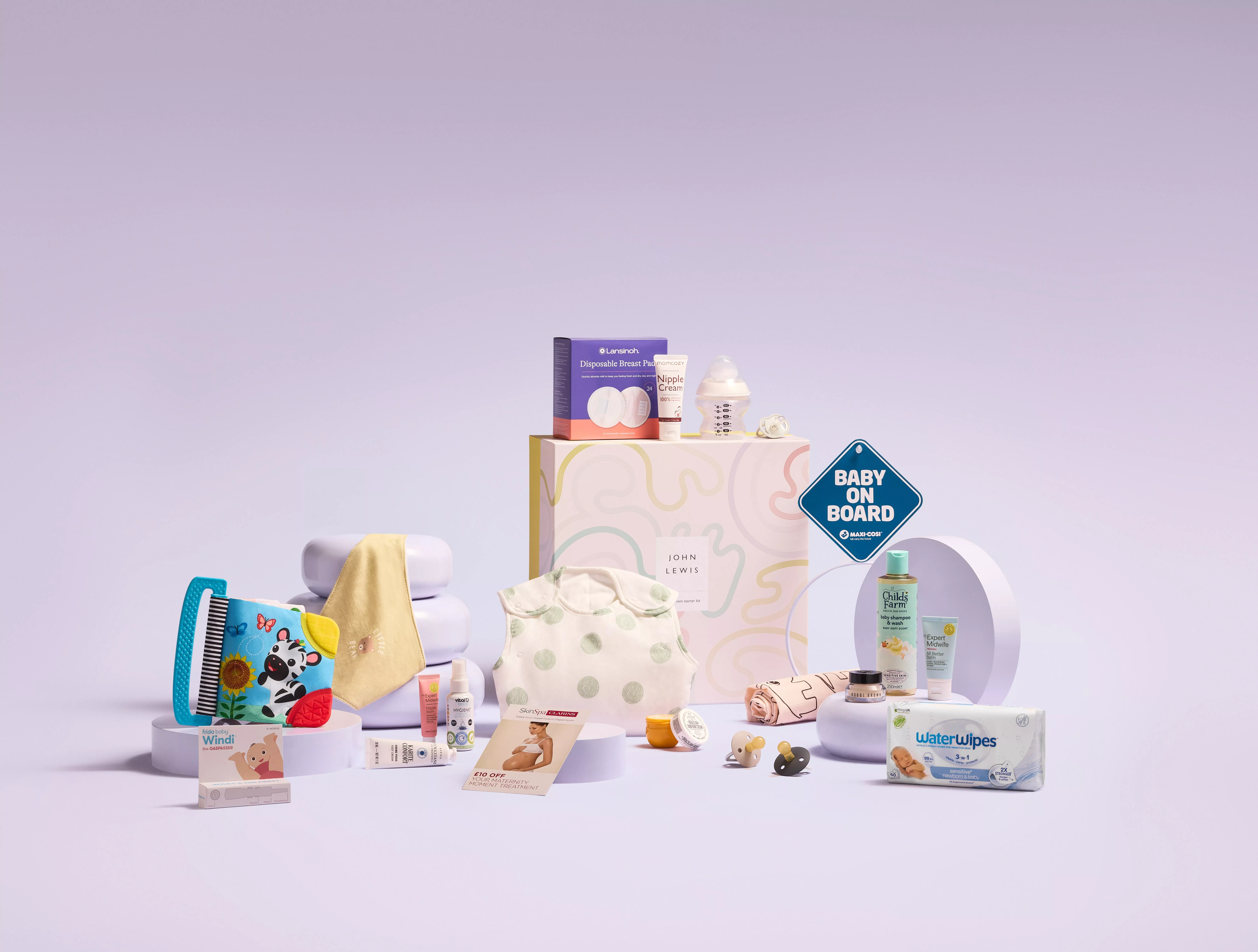 A collection of newborn essentials arranged on light purple platforms against a lilac background.