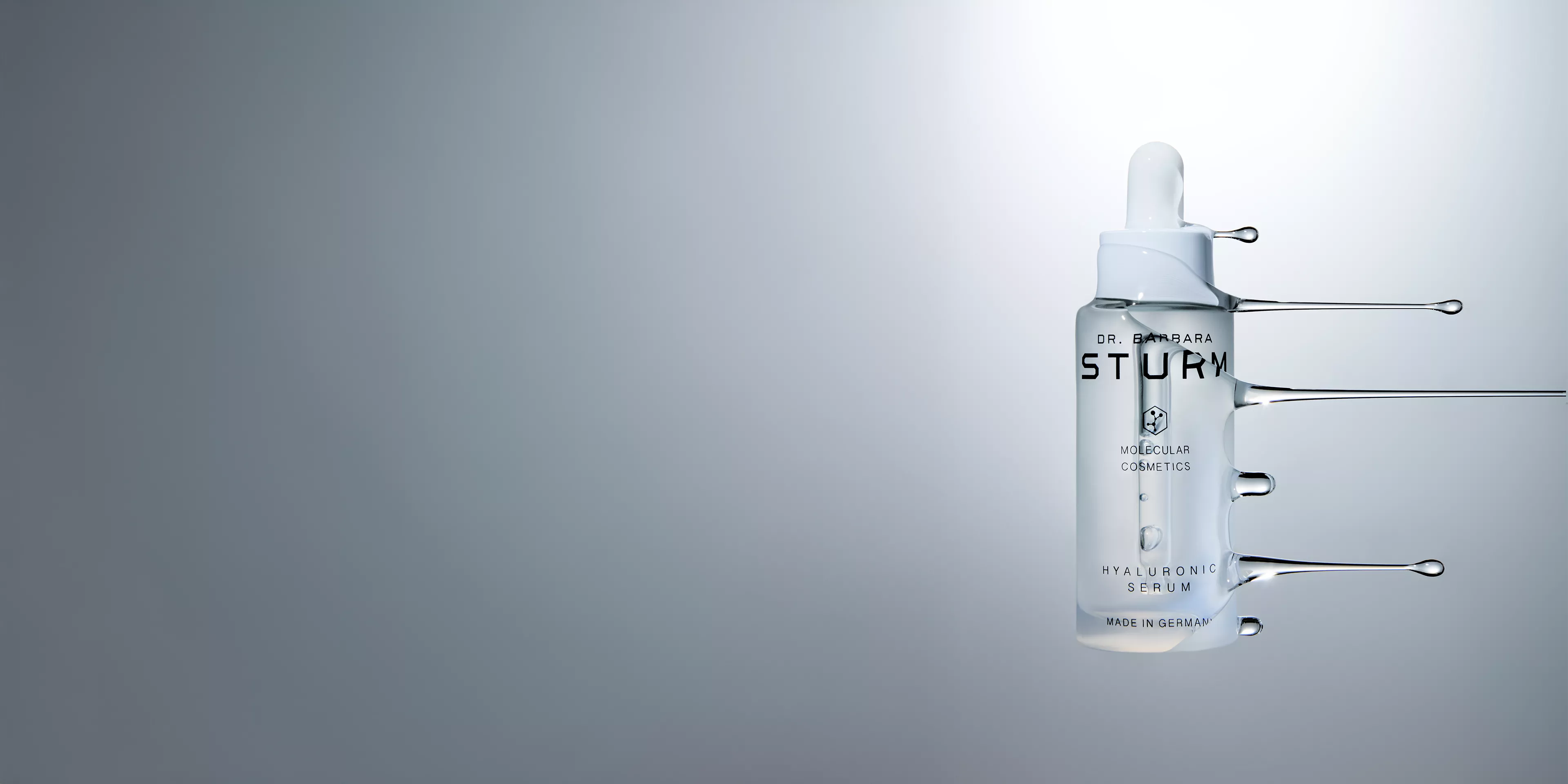 A bottle of Dr. Barbara Sturm Hyaluronic Serum centered against a soft grey gradient background.
