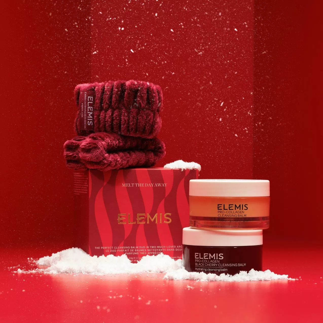 ELEMIS Pro-Collagen Cleansing Balm set with gift box, stacked jars, and plush red spa headbands set against a snowy red backdrop.