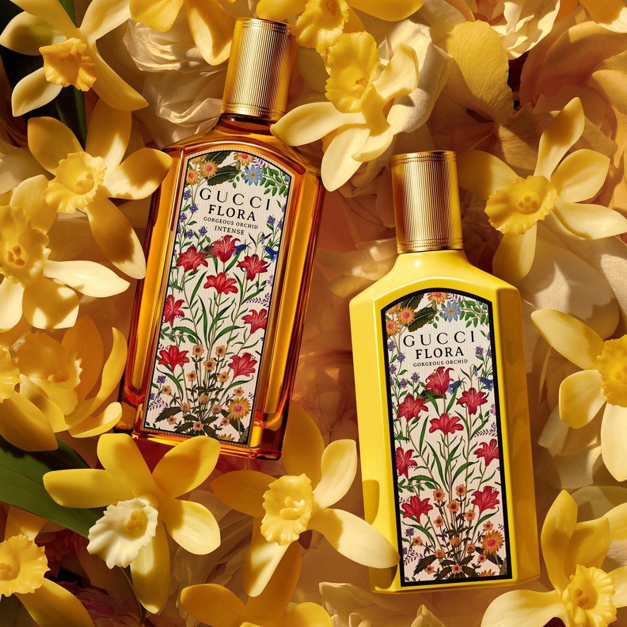 Two Gucci Flora perfume bottles—one clear glass and one opaque yellow—nestled among vibrant yellow orchid blossoms.