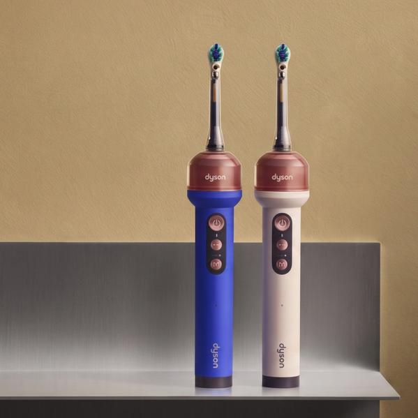 Two Dyson electric toothbrushes on a bathroom shelf, blue and white models with brush heads on beige wall background