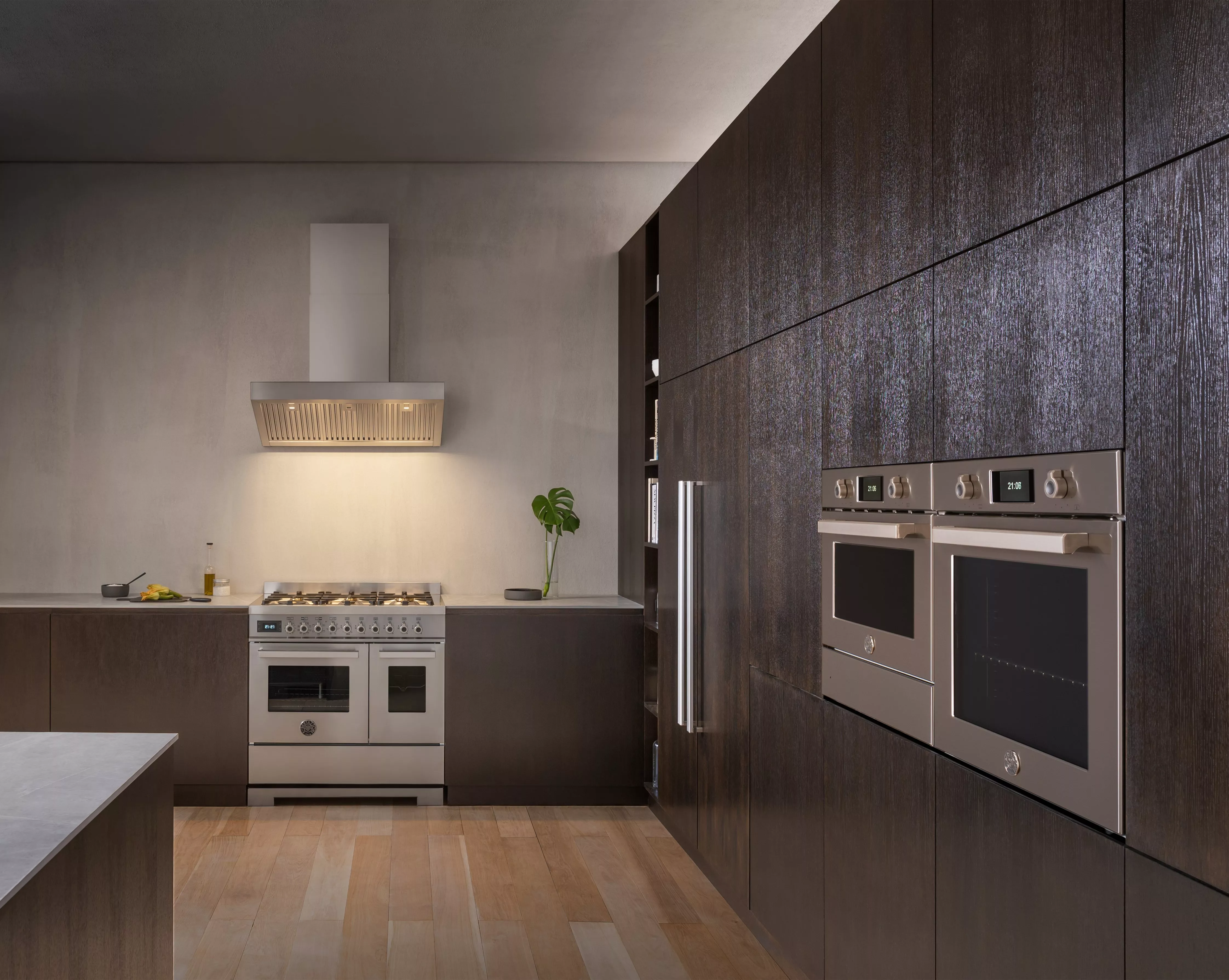 Modern luxury kitchen with stainless steel range cooker, twin built-in ovens and dark wood cabinets on light timber flooring