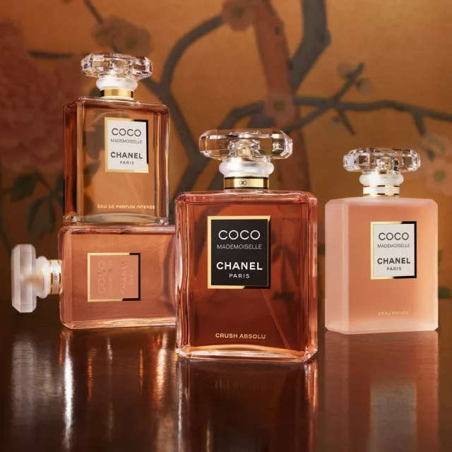 Chanel Coco Mademoiselle perfume bottles on reflective table, luxury fragrance display in warm lighting.