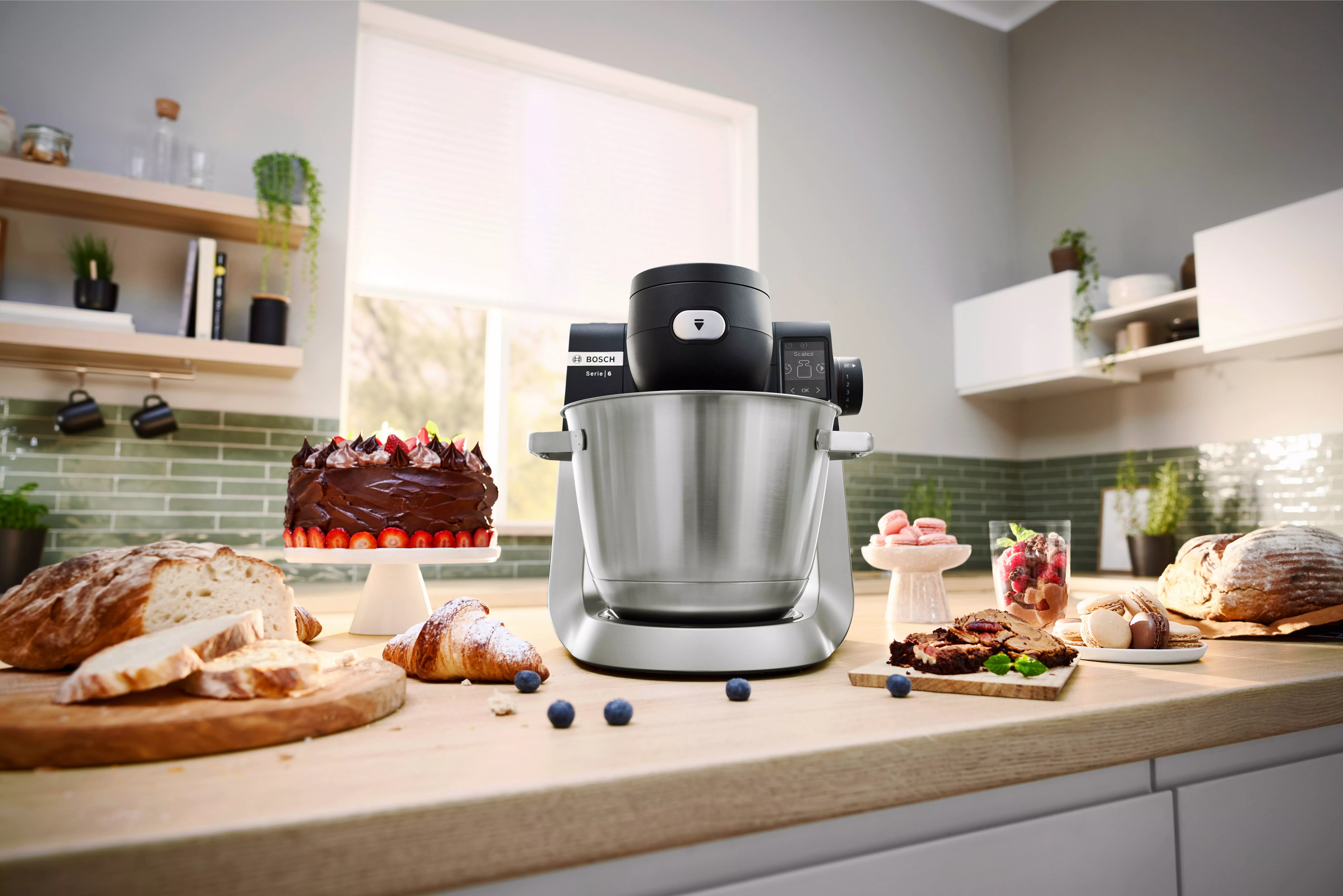 A modern kitchen with a Bosch mixer surrounded by delicious homemade cakes, bread, and pastries on a wooden countertop.