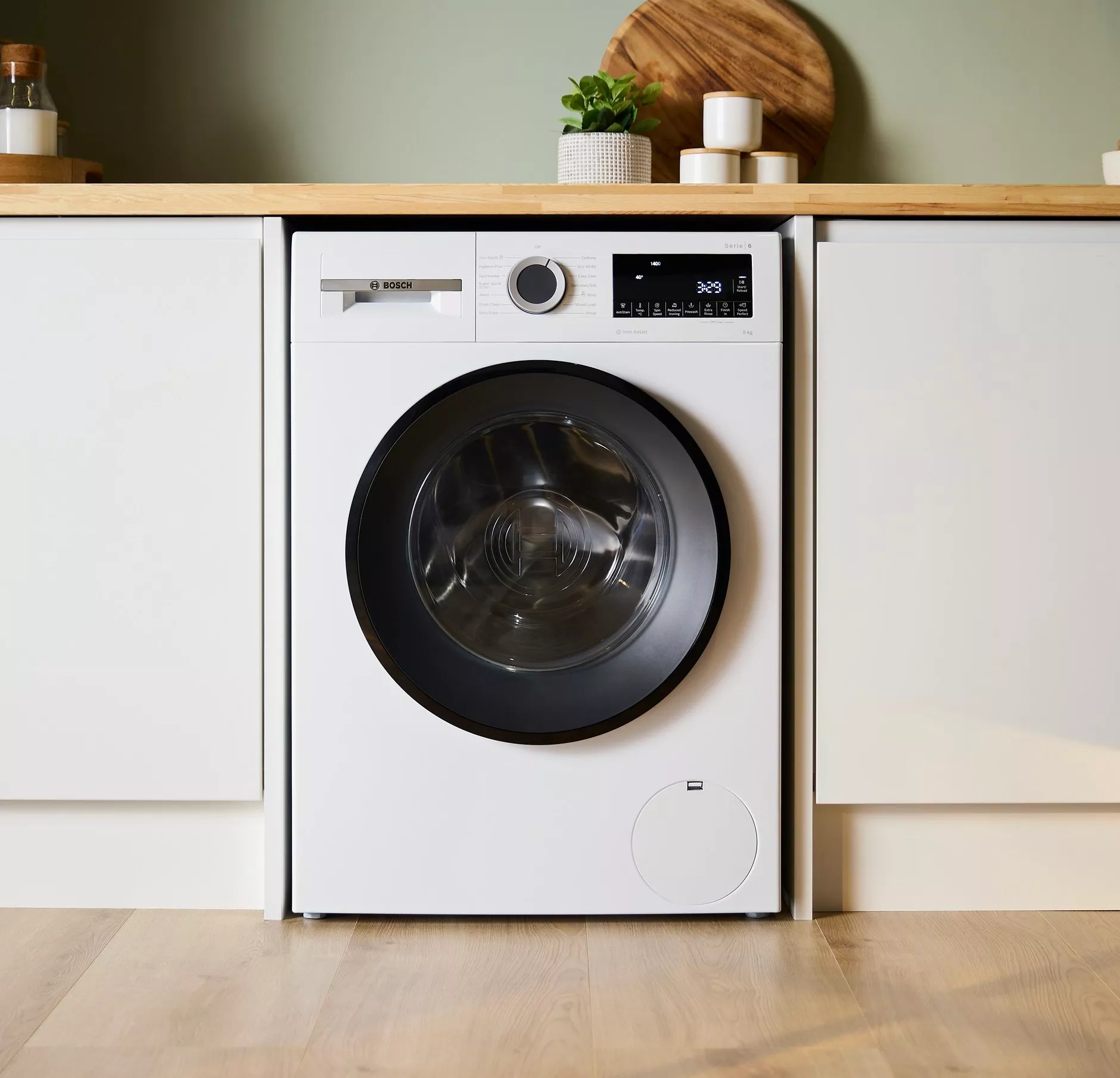 A Bosch washing machine with a digital display and control dial, topped by a stack of colourful folded clothes.