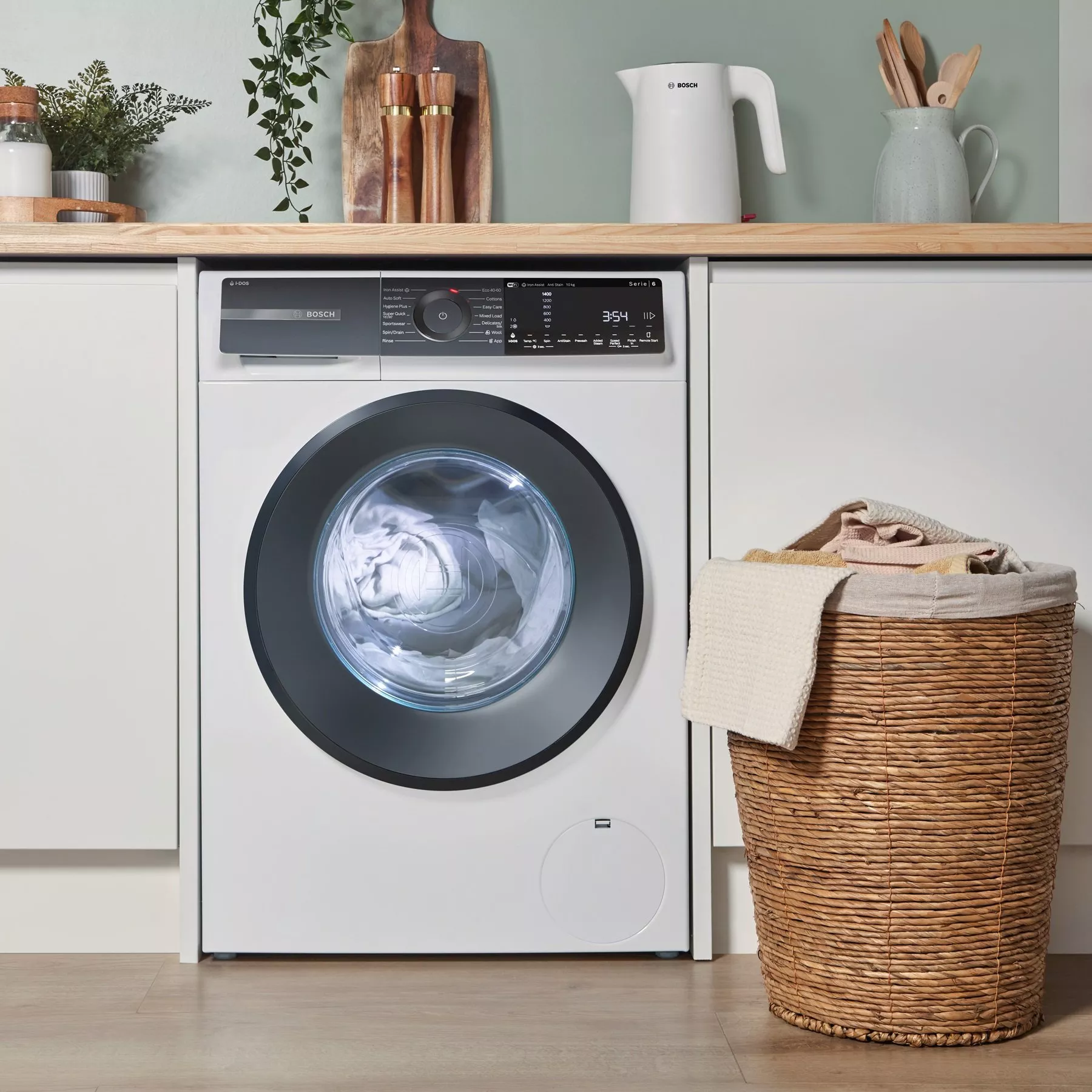 Bosch front-loading washing machine in modern utility room with wooden worktop, plants and wicker laundry basket