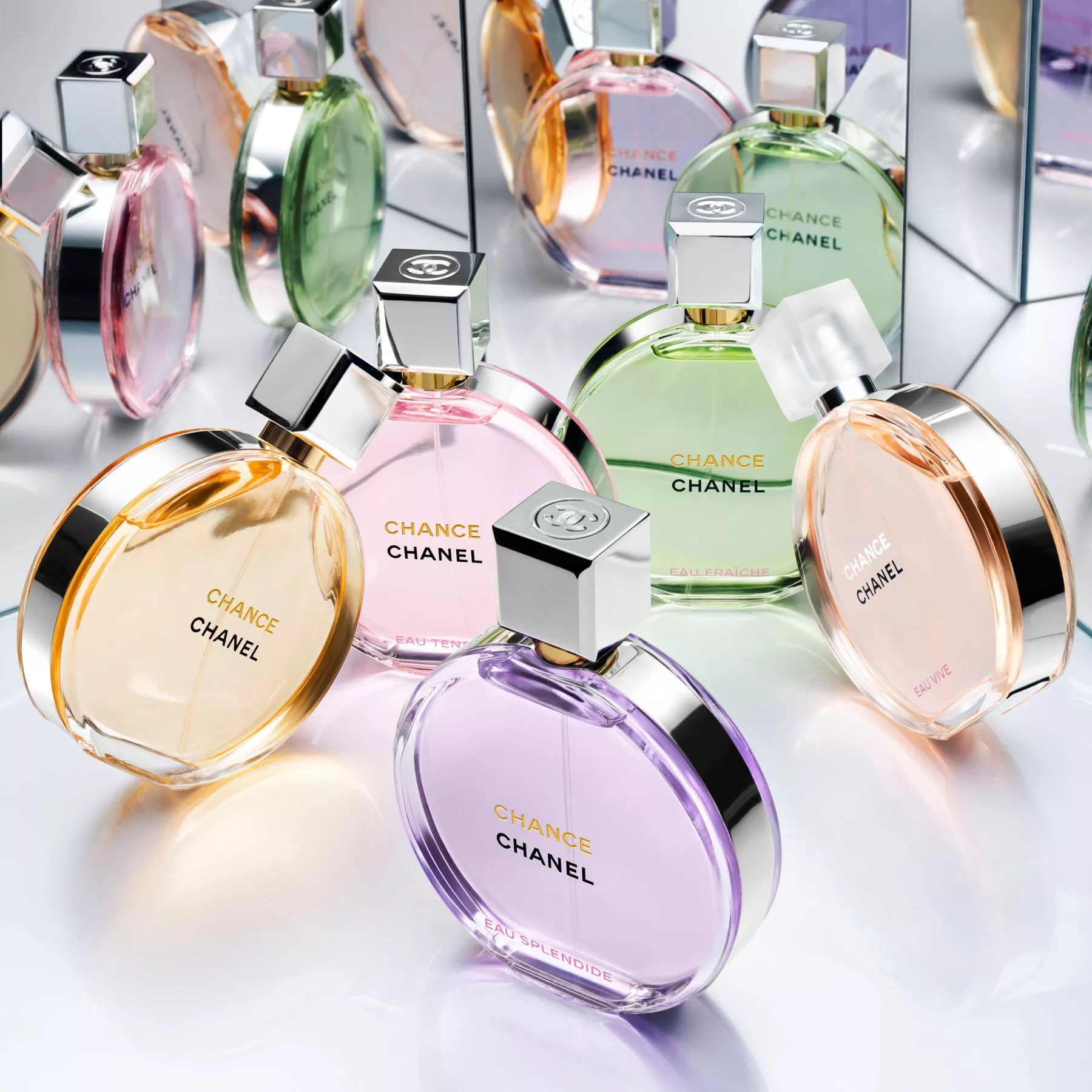 An array of colorful, round CHANEL CHANCE perfume bottles in shades of pink, green, yellow, and purple are artistically arranged on a reflective surface with mirror backgrounds