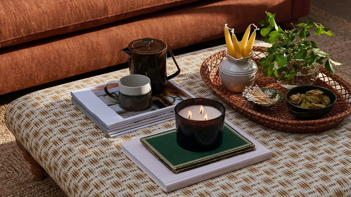 three wick candles on a footstool with coffee pots, books and other candles