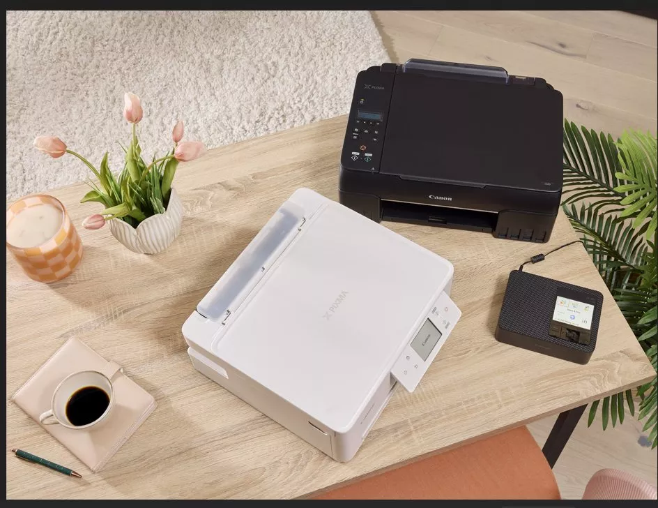 Modern office setup with two printers, a small device, coffee, and pink tulips on a wooden desk.