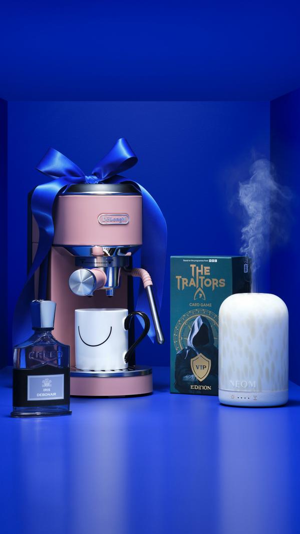 Pink De’Longhi espresso machine gift set with mug, Creed perfume, Traitors card game and NEOM diffuser on blue backdrop