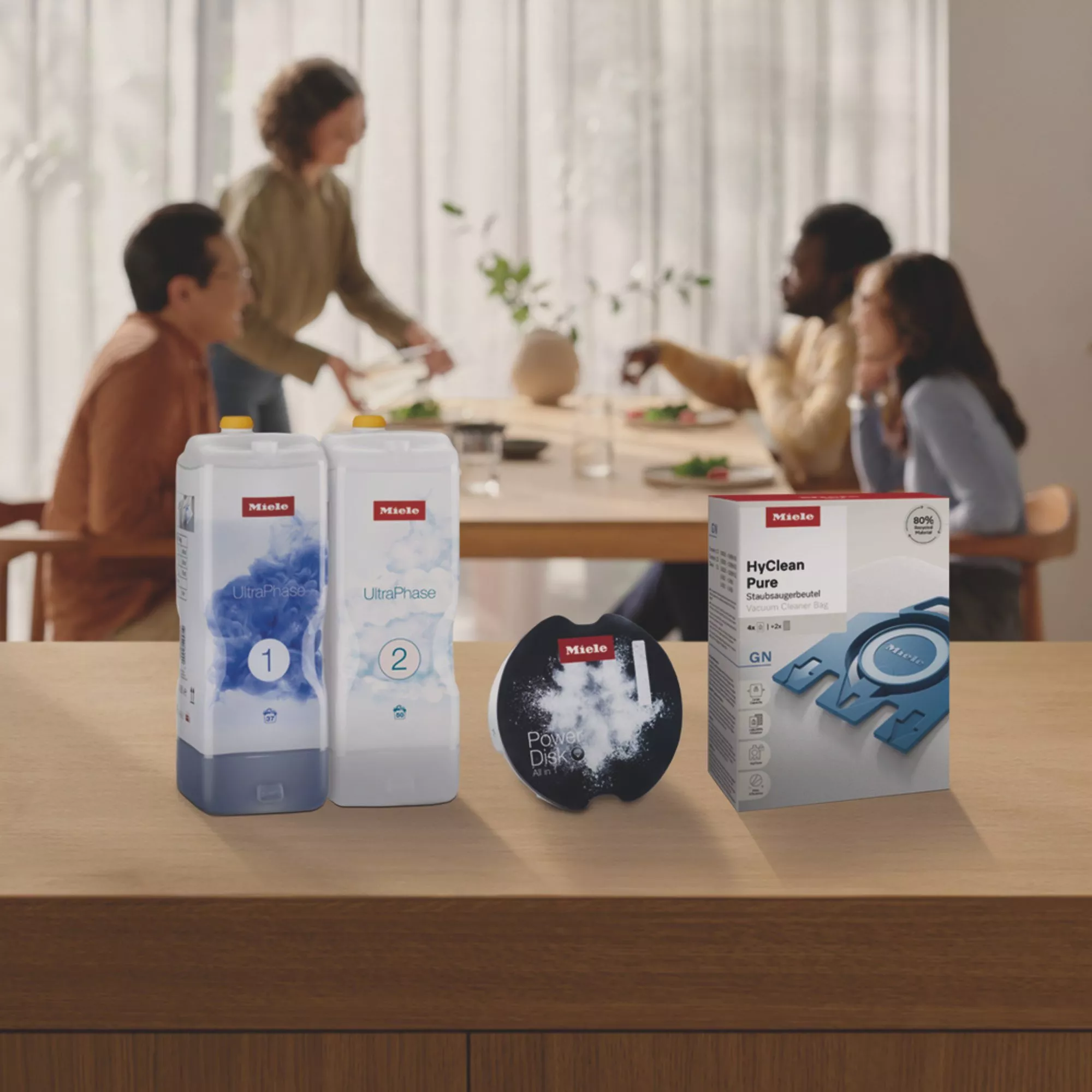 Miele UltraPhase detergents, PowerDisk and HyClean Pure vacuum bags on kitchen counter, family dining in soft-focus 