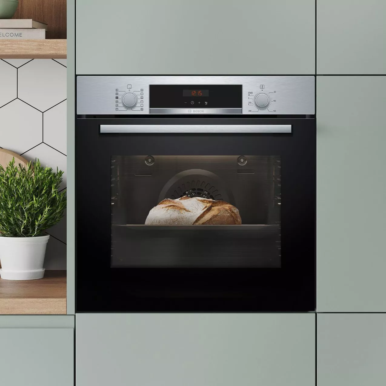 A built-in Bosch stainless steel and black glass oven baking a loaf of bread, integrated into sage green kitchen cabinetry.