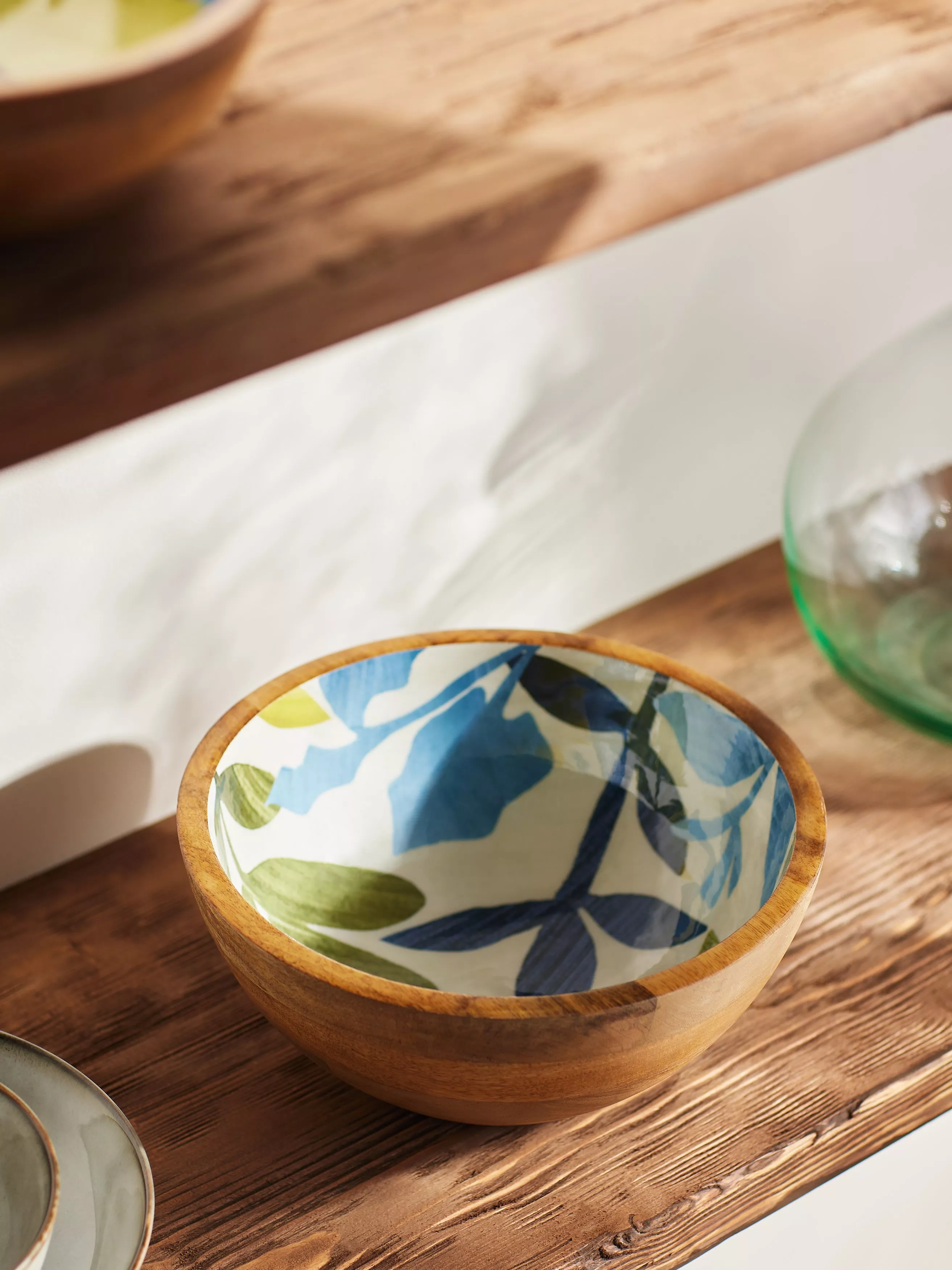 Colourful patterned ceramic bowl on a kitchen shelf, featuring blue geometric tiles and floral design in sunlight