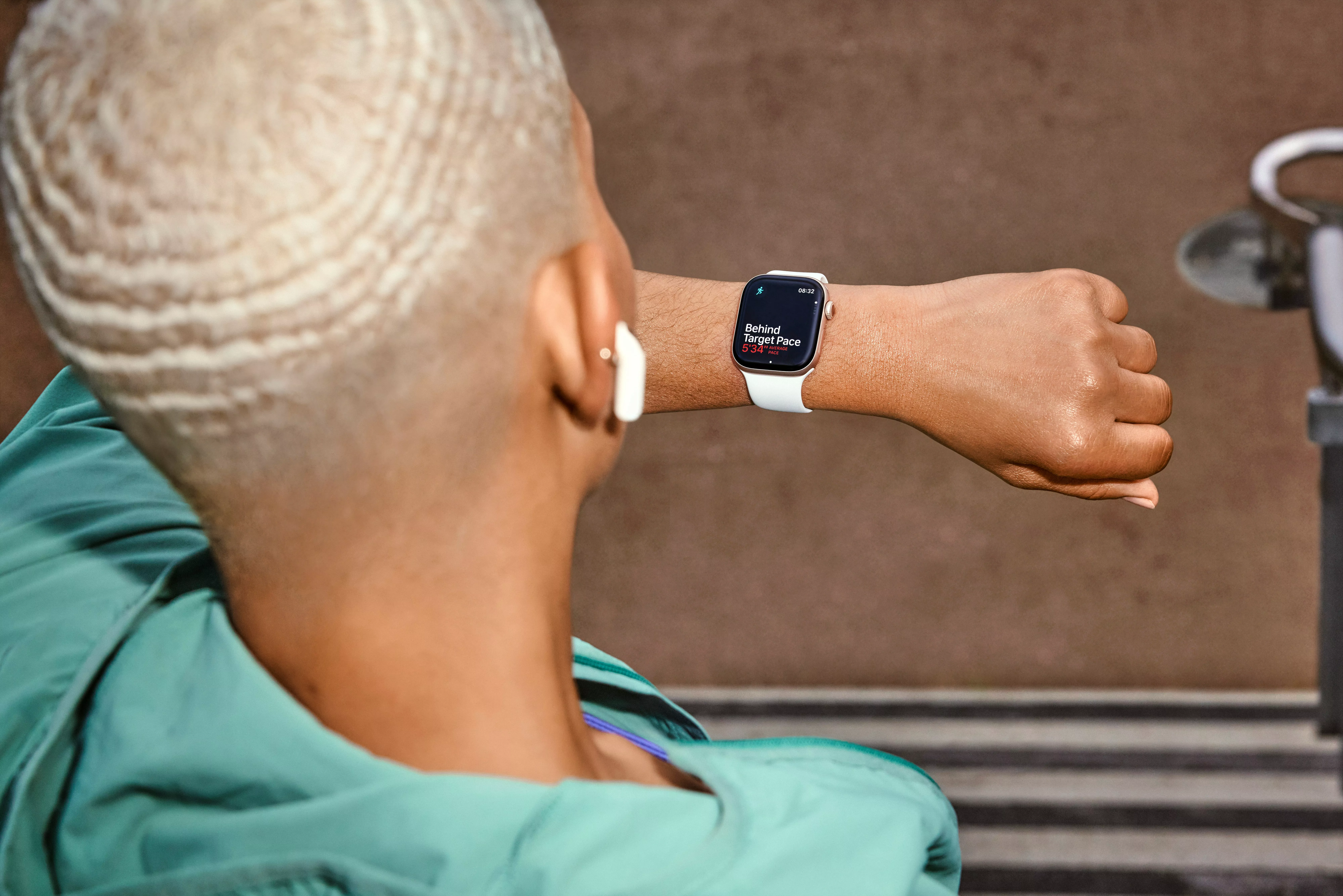 Runner checking smartwatch pace and workout stats on a treadmill, wearing wireless earbuds at the gym