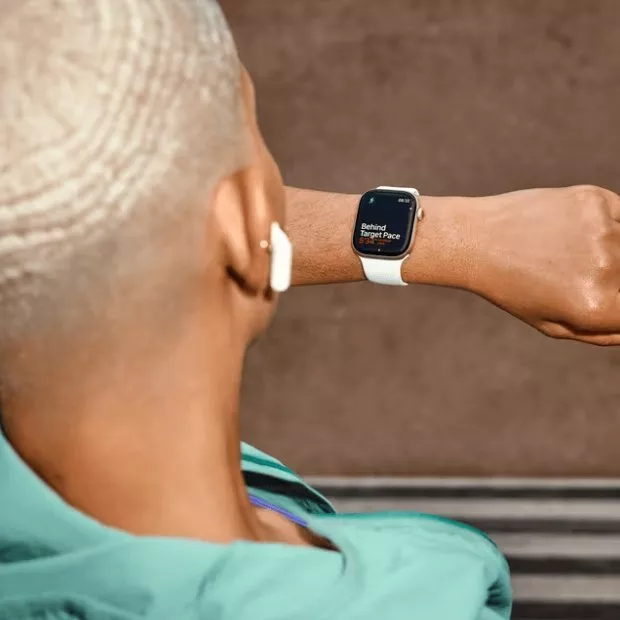 Runner checking smartwatch pace during outdoor workout, wearing wireless earbuds and teal sports top