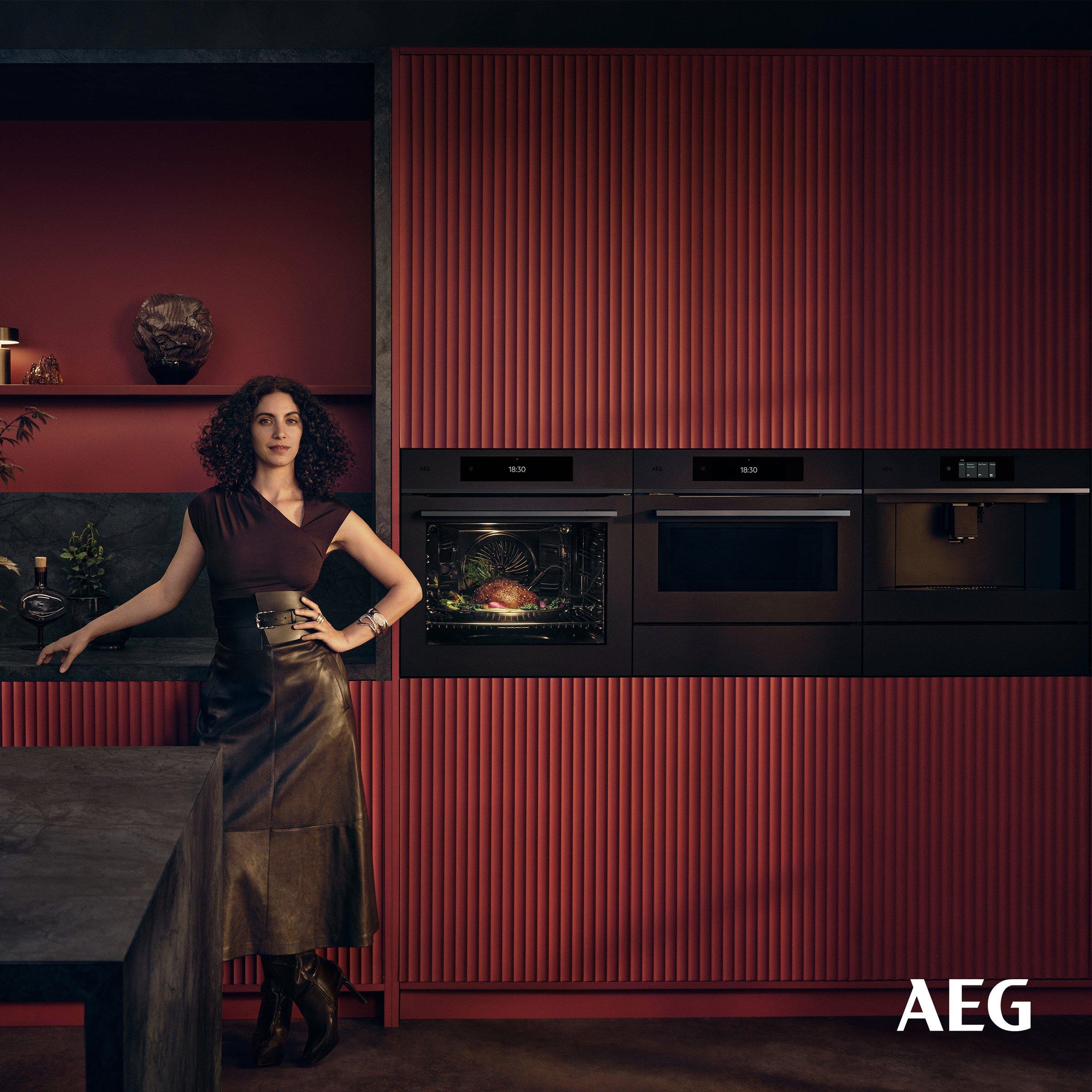 A confident woman wearing dark brown top and a high-waisted leather skirt in a modern kitchen showcasing age an oven, a microwave, and a coffee machine