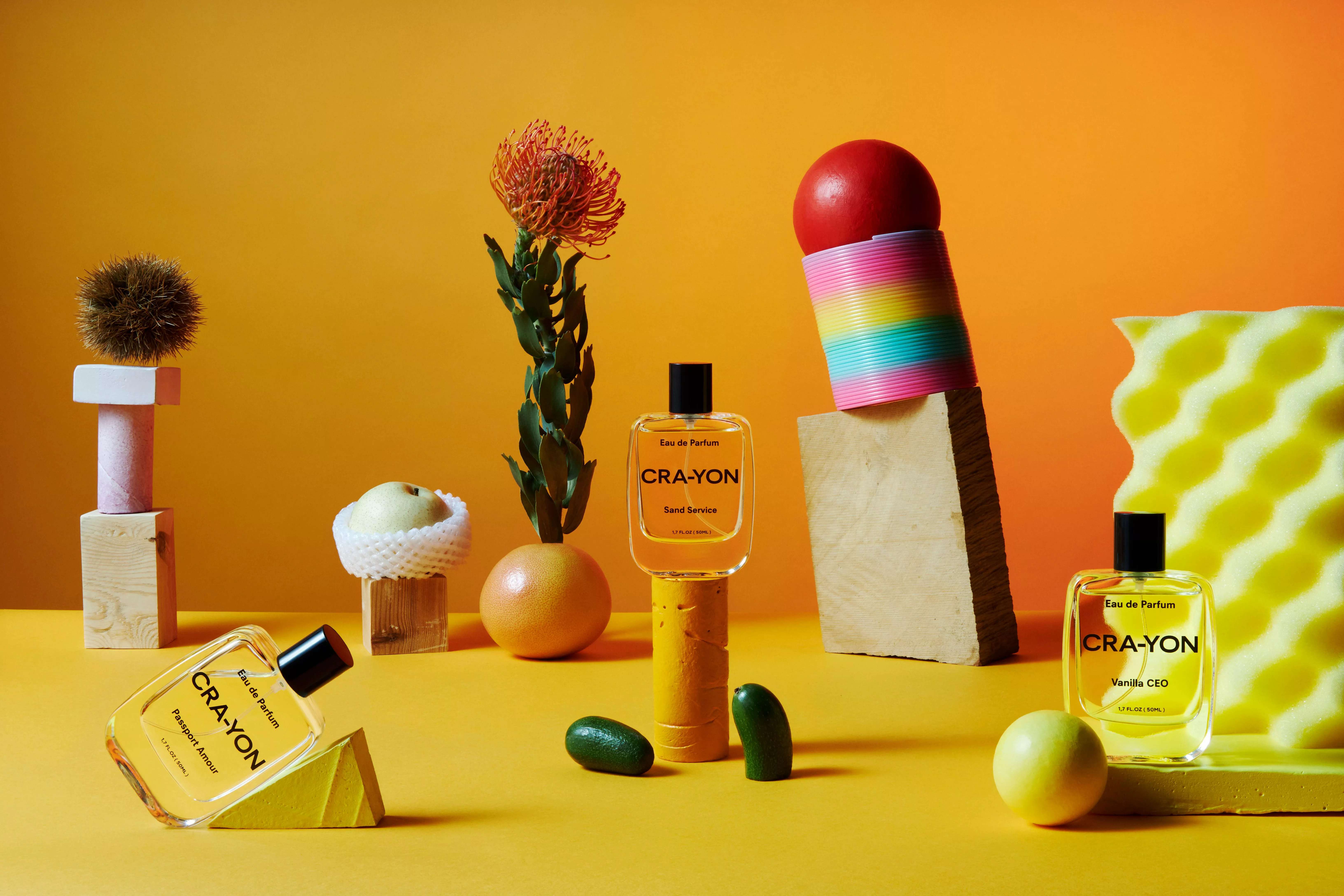 CRAYON eau de parfum bottles in colourful still life with fruit, flower and props on orange background