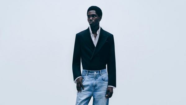 Fashion portrait of a man in black blazer and white shirt with light blue jeans against a clean studio backdrop
