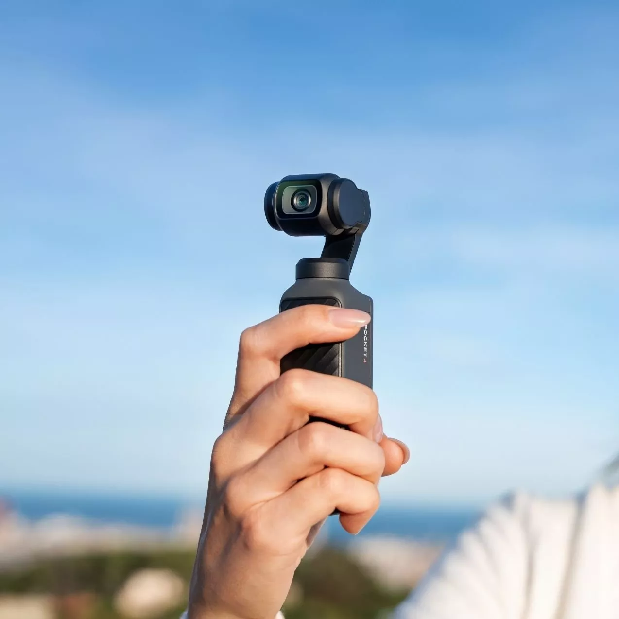 Hand holding a compact handheld gimbal camera for stabilised vlogging and travel filming against blue sky