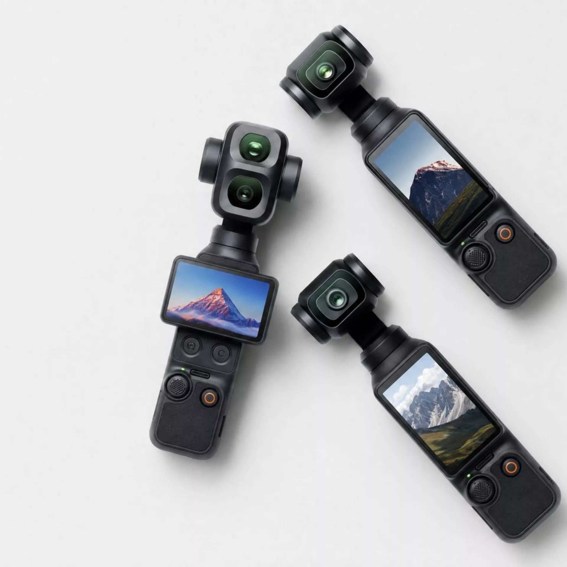 Three handheld gimbal action cameras with touchscreen displays showing mountain landscapes on a white background