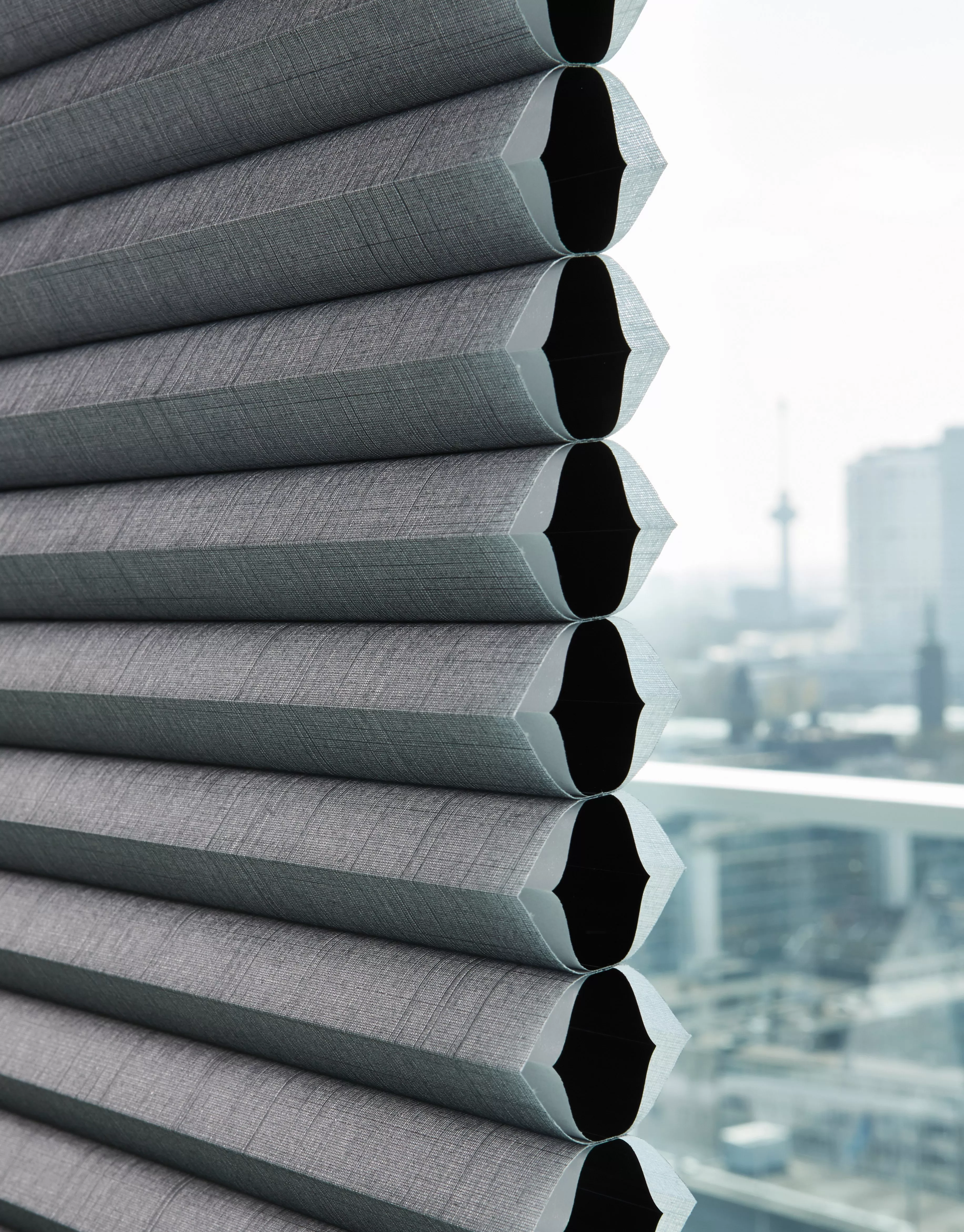 Close-up of grey cellular honeycomb blinds on window, with soft-focus city skyline in background