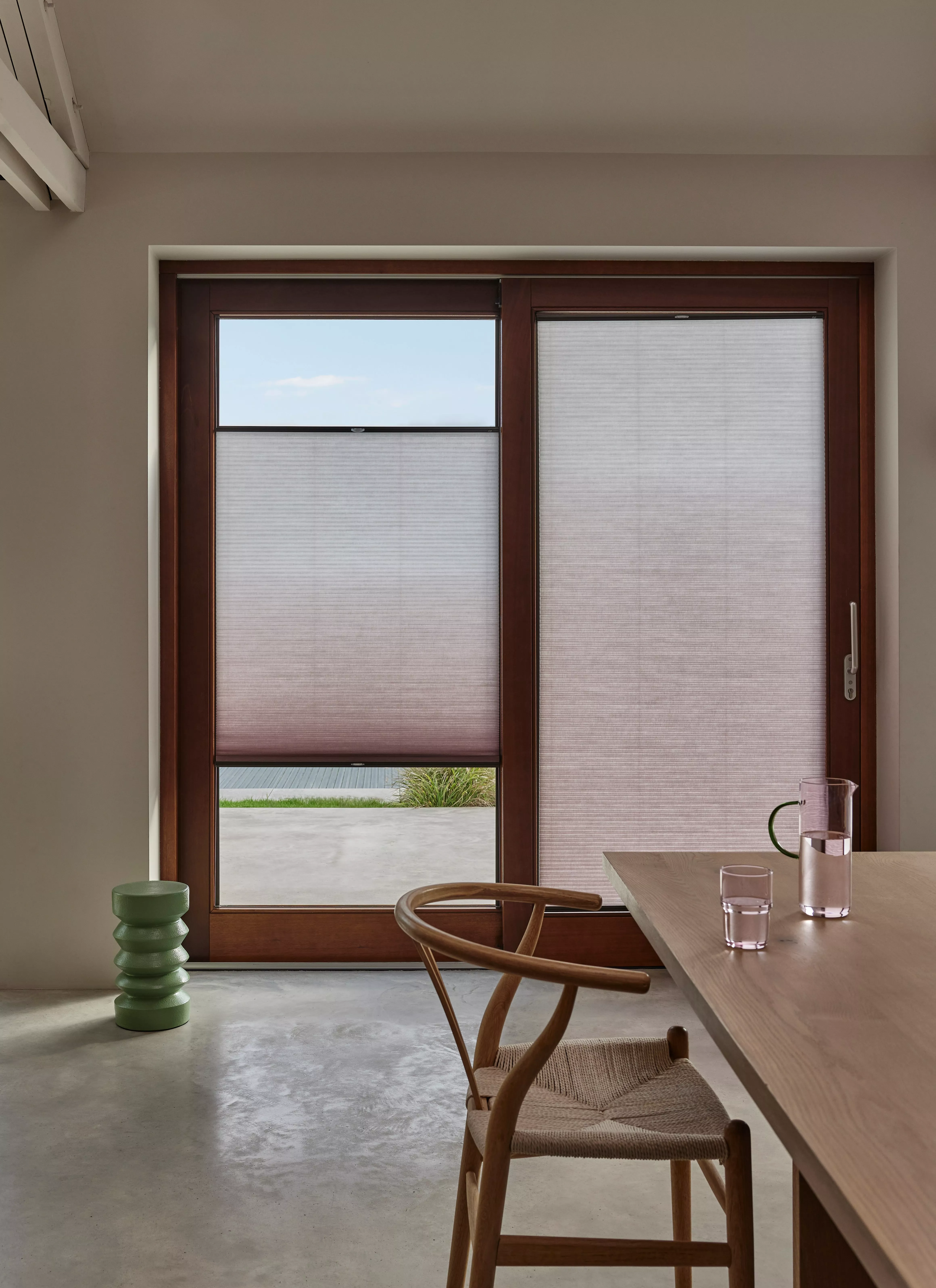 Modern dining room with wooden sliding doors and pleated blinds, minimalist table, chair and water jug.