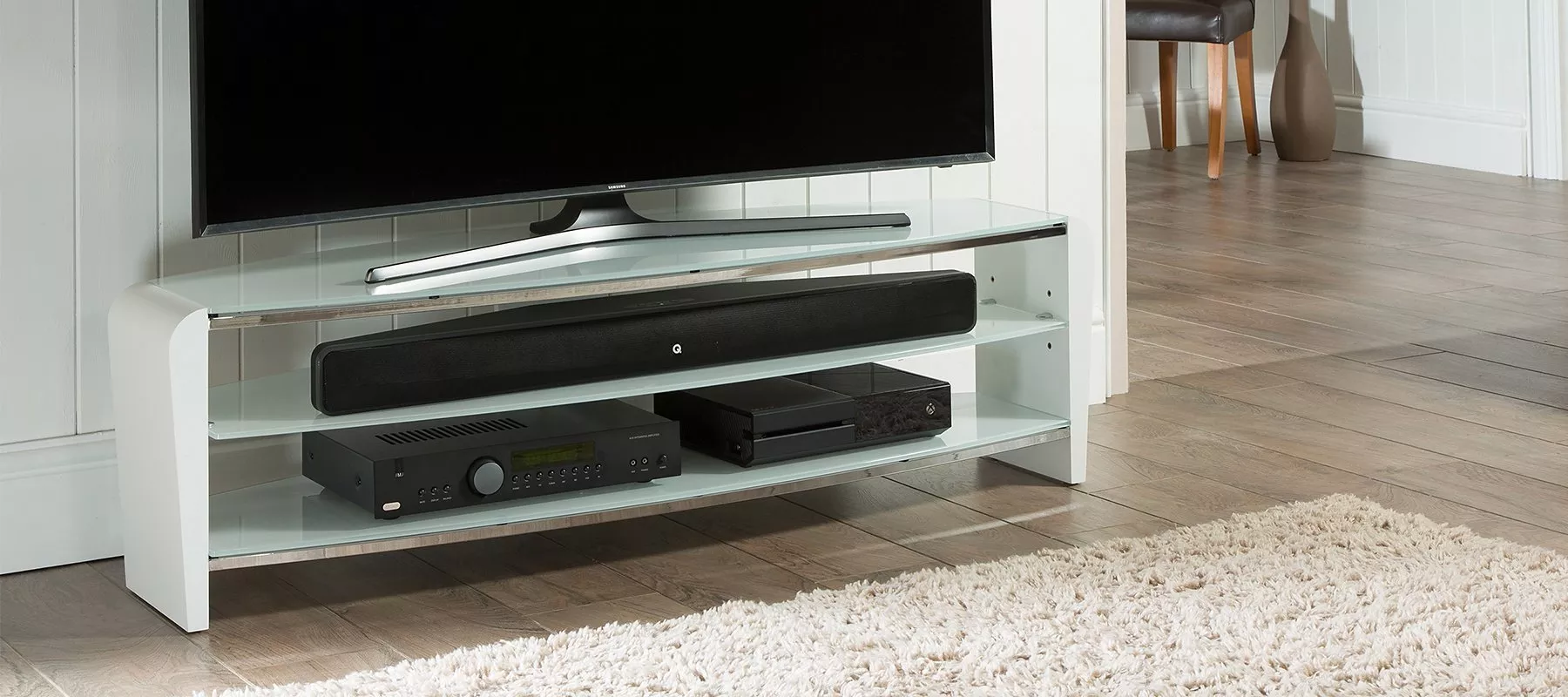 Modern living room with sleek TV stand holding a flat-screen TV, soundbar, and electronic devices, on wooden floor.