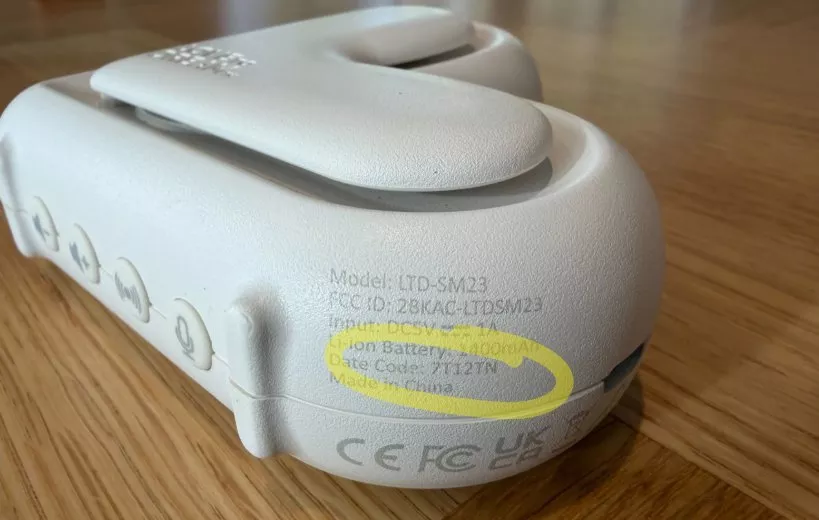 Close-up of grey electronic device on wooden table, showing model label, battery info and control buttons