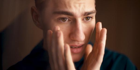Close-up portrait of a young man holding his face, concerned expression watching the football
