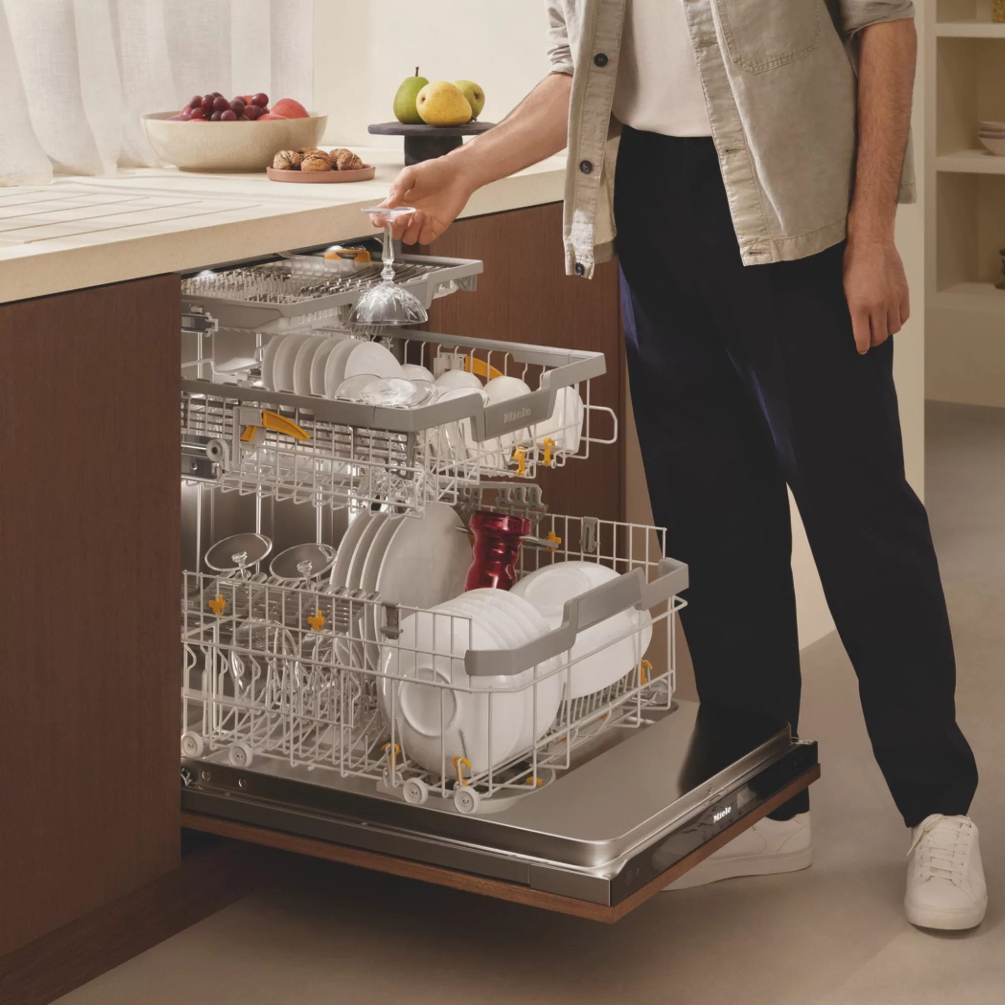 Person loading built-in dishwasher with plates, glasses and cutlery in modern kitchen for efficient dishwashing and cleaning