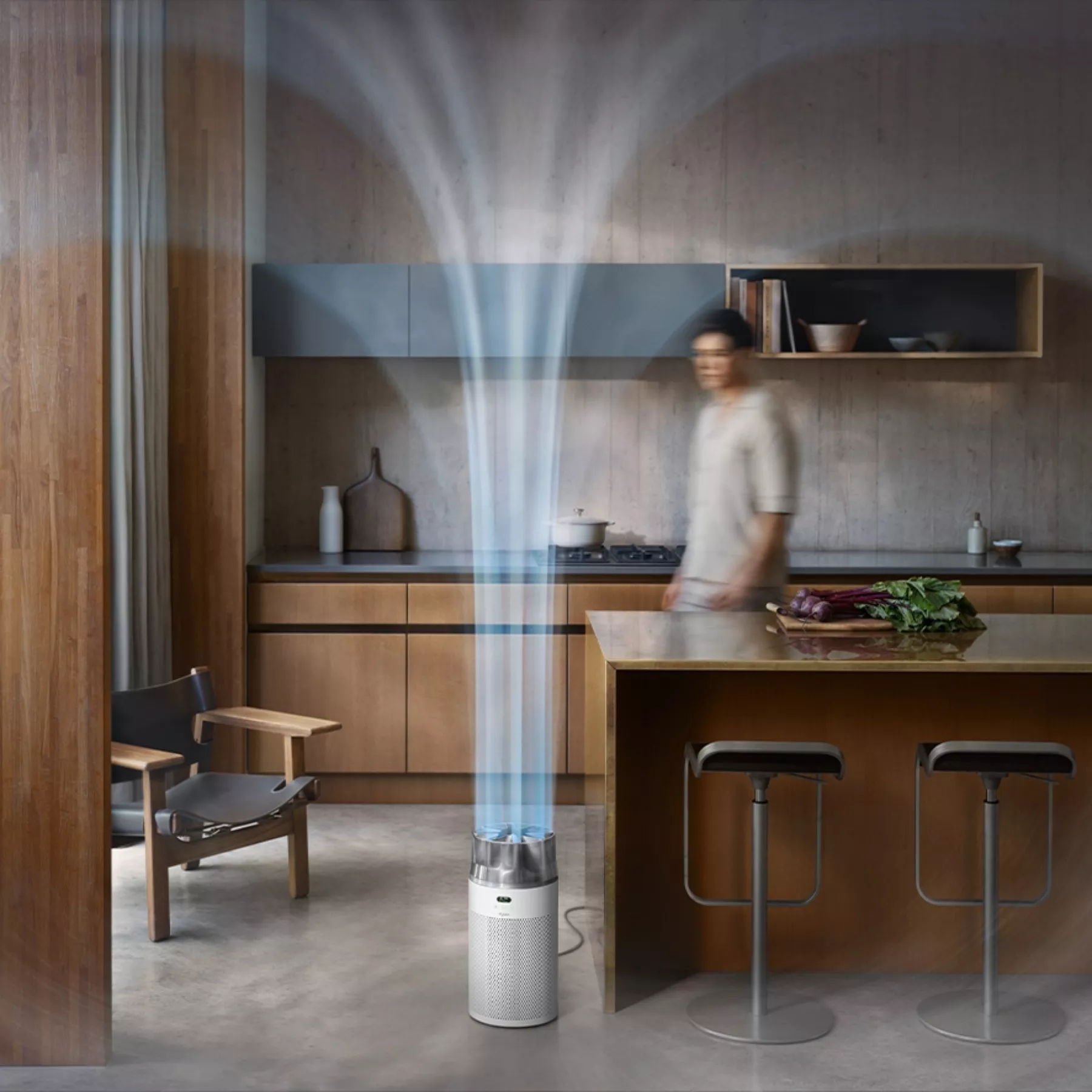 Modern kitchen with a sleek air purifier filtering air. Wooden cabinetry and counter with fresh vegetables visible.