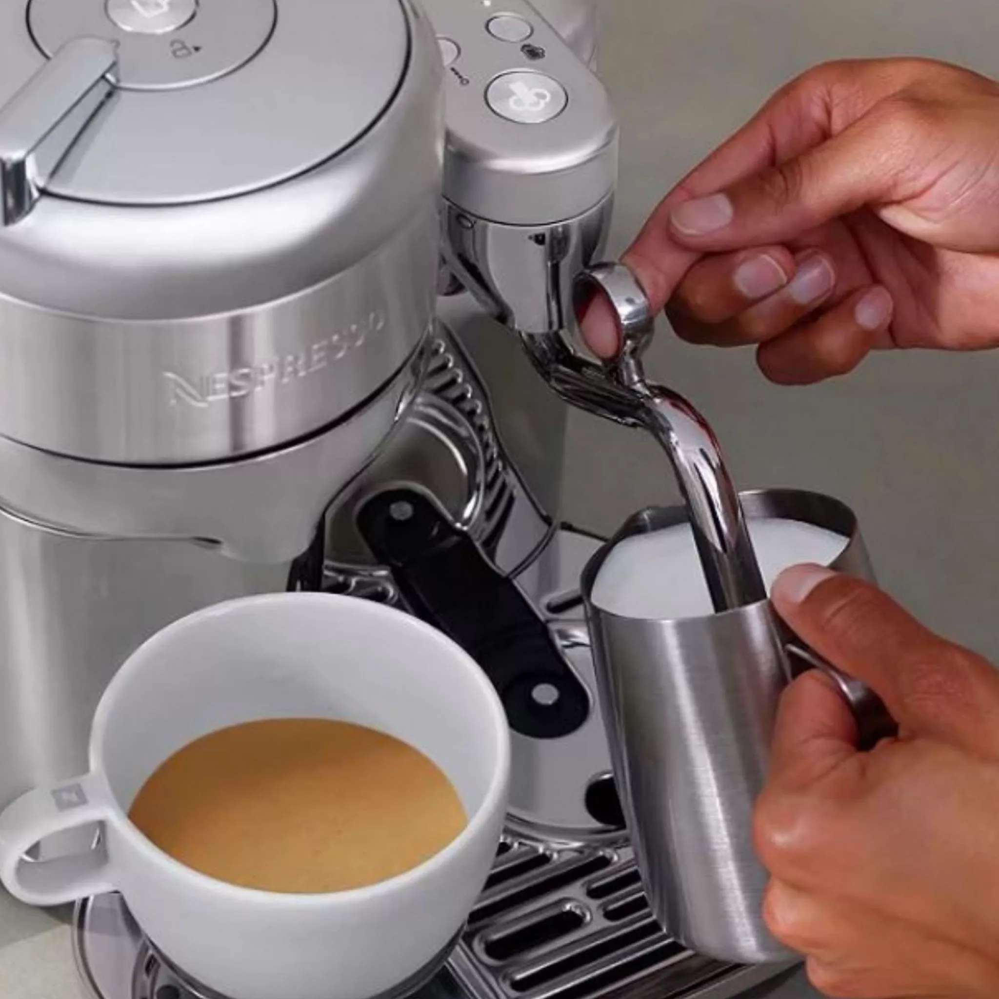 Nespresso machine with espresso shot and person frothing milk in a jug