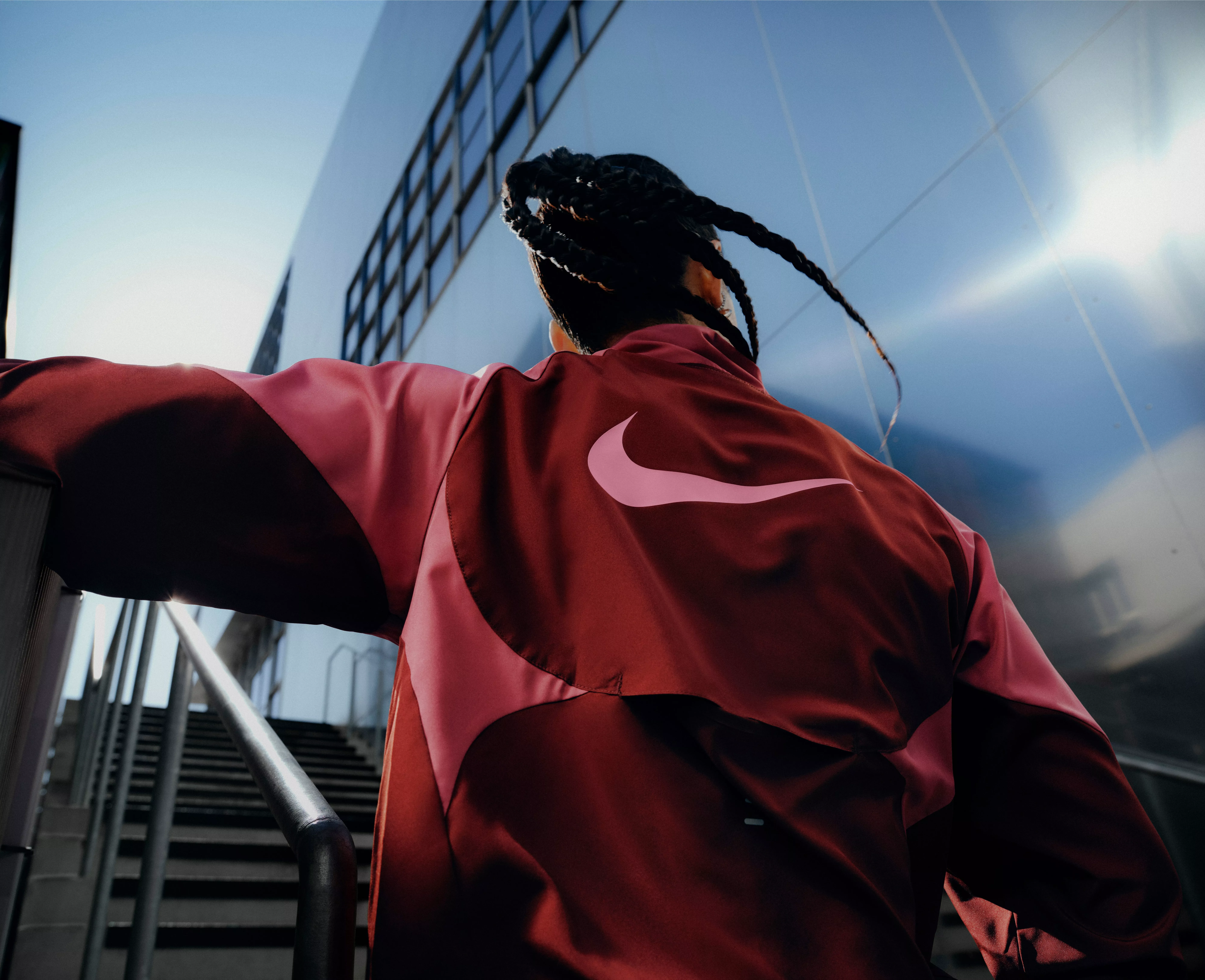 Athlete in red Nike jacket climbing outdoor stairs beside modern glass building, urban fitness training view